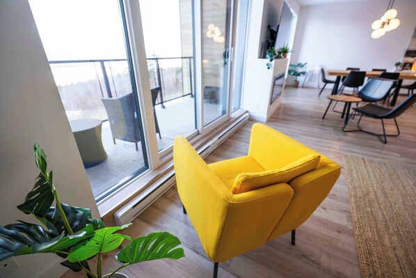 A modern interior with a yellow armchair, large windows, and a dining area. - 210 | Chic Escape | View & Comfort with Pool (Baie-Saint-Paul)