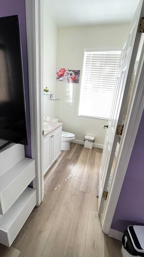 A compact bathroom with a toilet, sink, and a glass shelf with decorative items. - A modern cozy home decorated with love (Lutz)