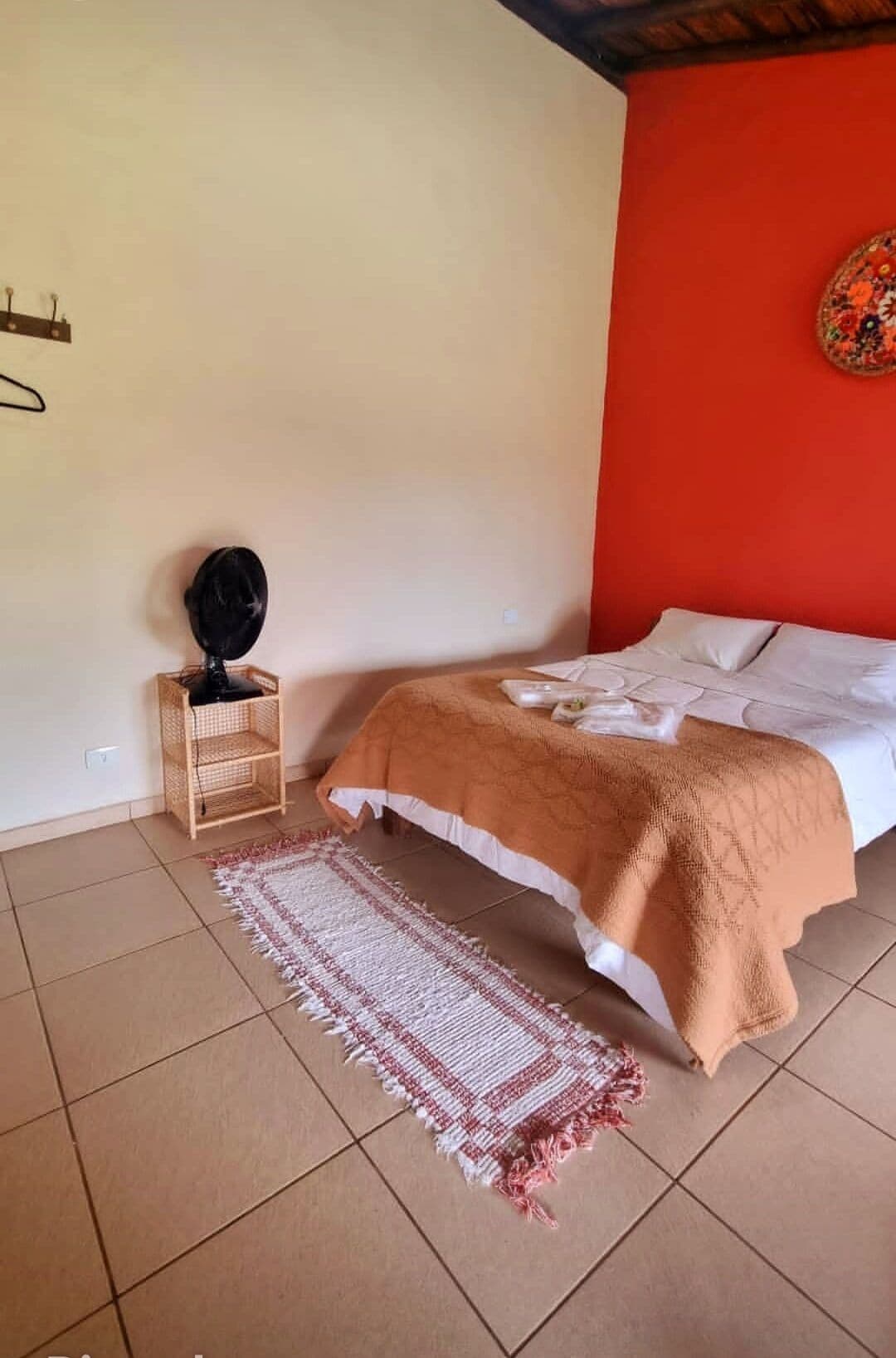 Une chambre à coucher avec un lit, une petite table de chevet, un tapis et un mur agrémenté d’un objet décoratif.