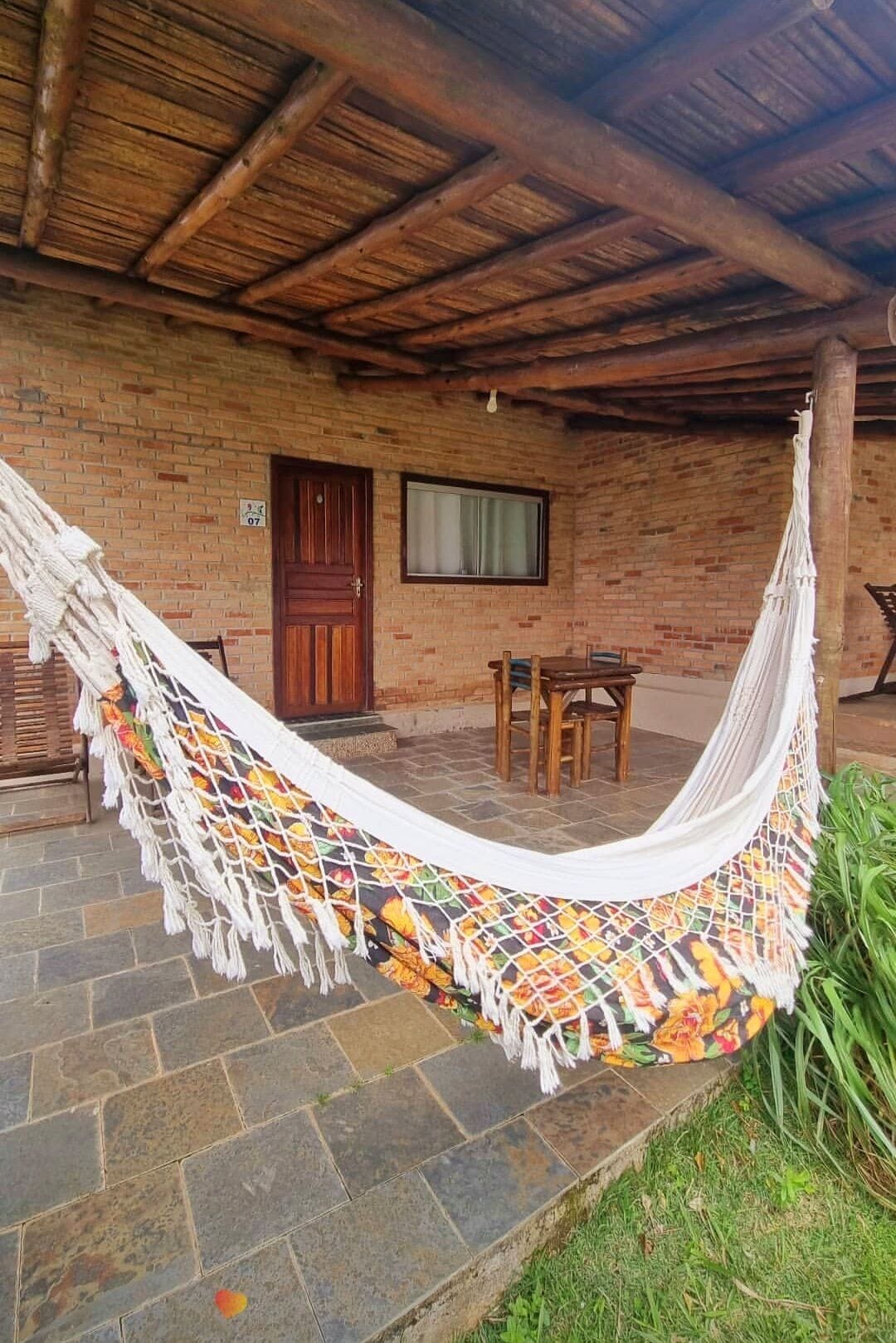 A hammock tied between two wooden posts, a brick building with a wooden door and window, and a stone-paved patio.