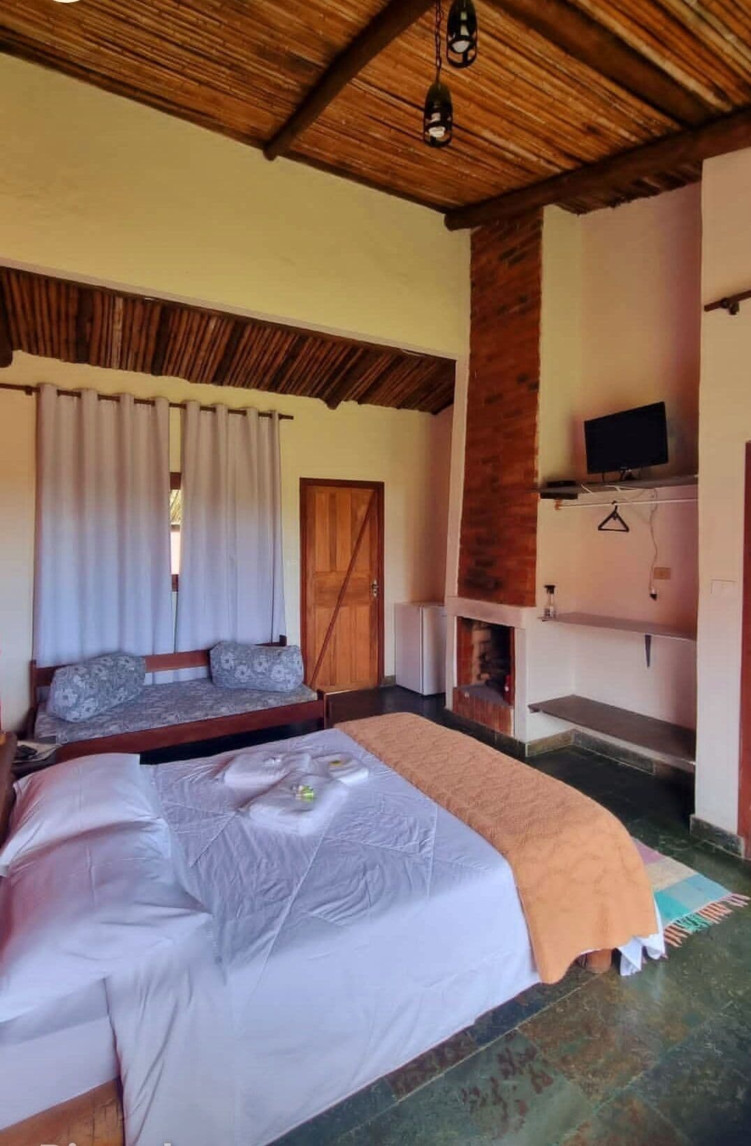 Quarto com cama, cortinas, televisão e lareira.