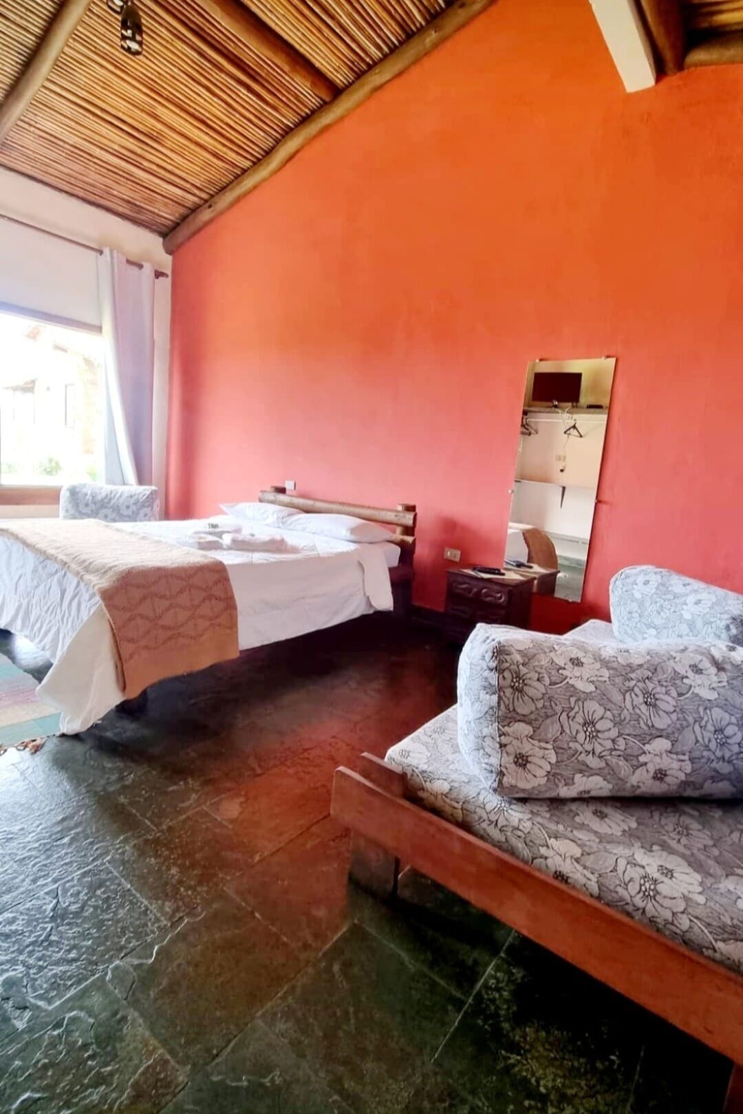 Quarto com duas camas, teto de madeira, parede vermelha e chão de azulejos.