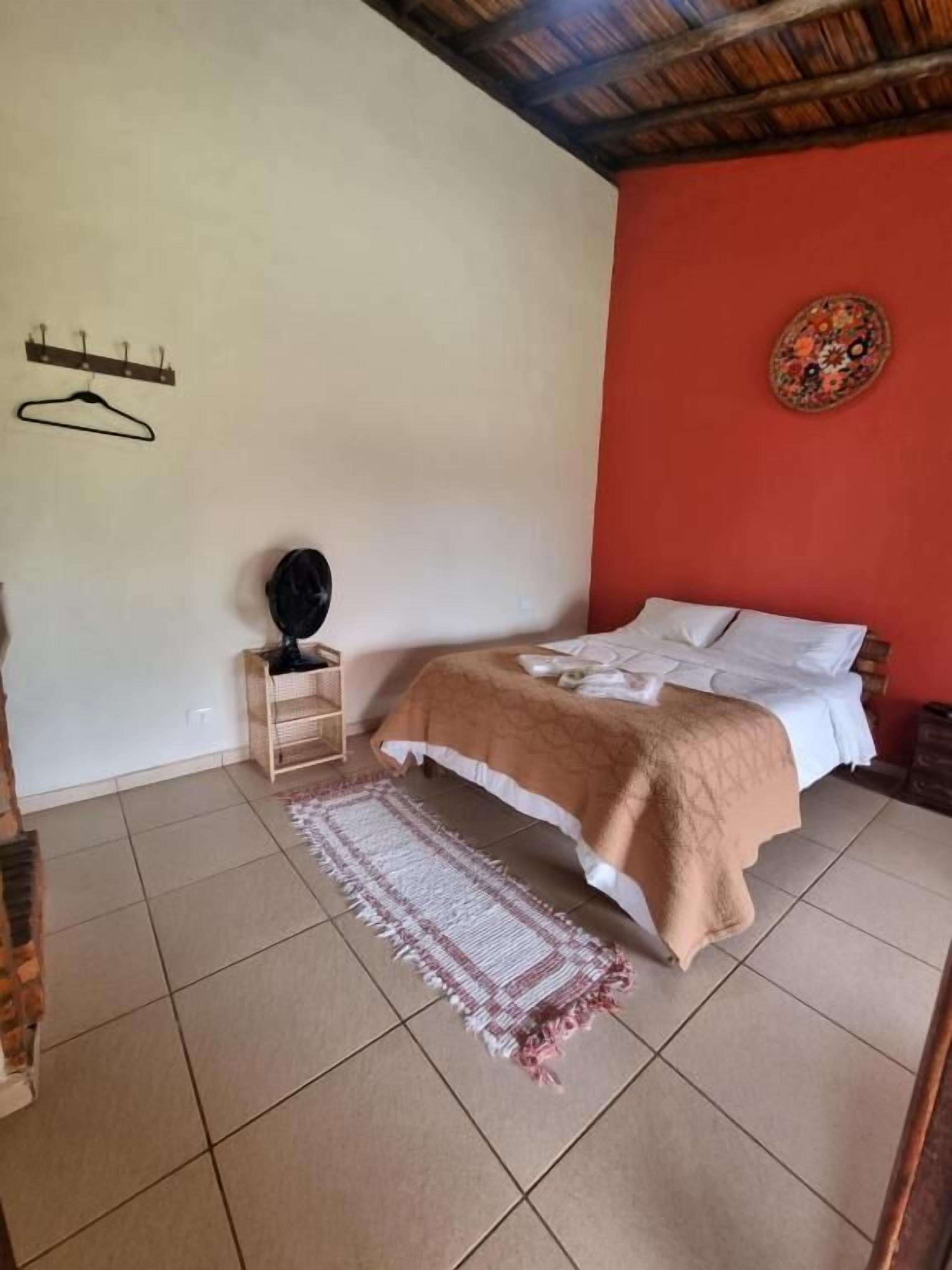 A bedroom with a bed, a hanging coat rack, a small wooden cabinet, and a decorative wall hanging.
