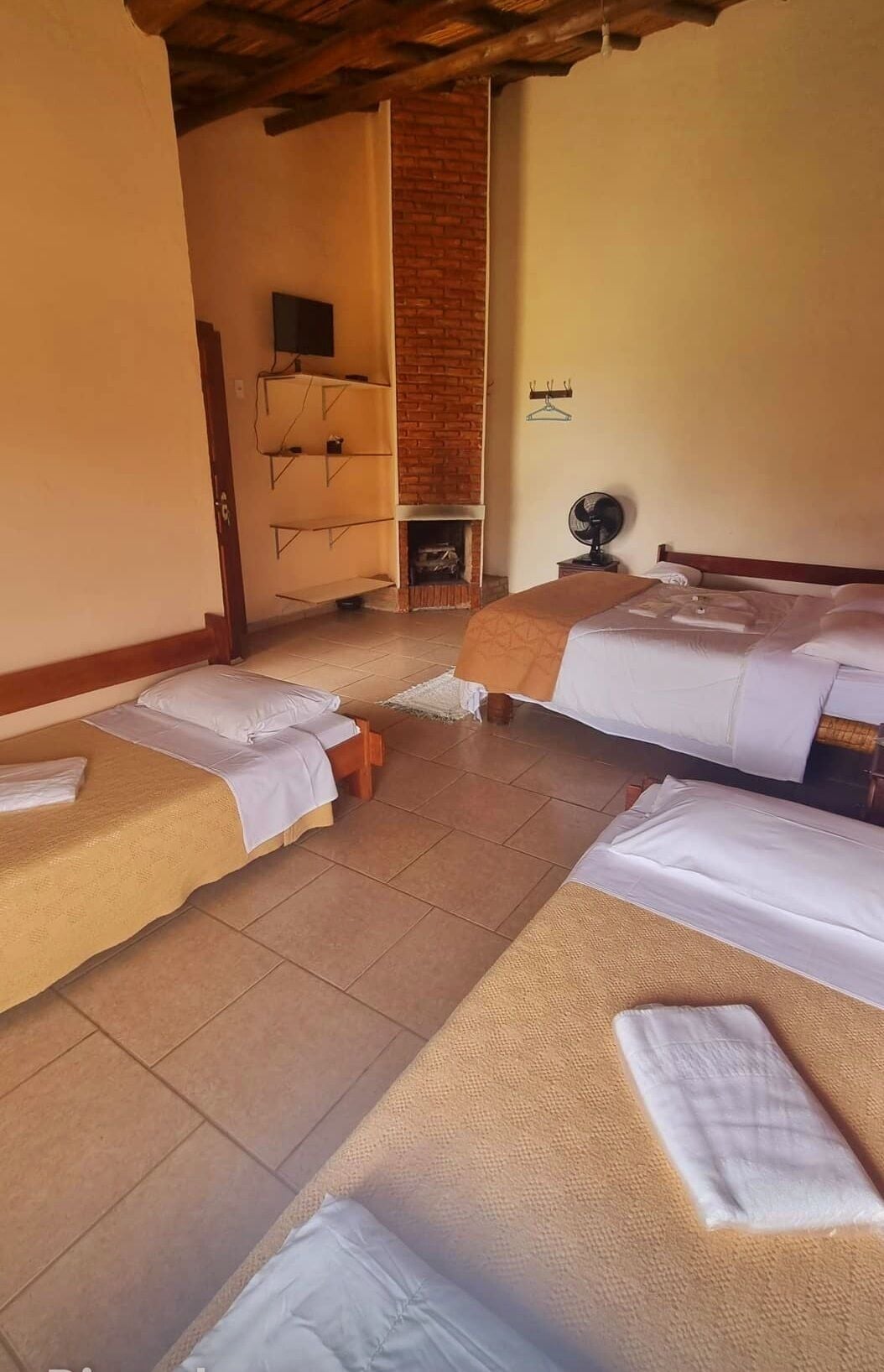 A hotel room with two beds, a brick fireplace, a wooden dresser, and a fan.