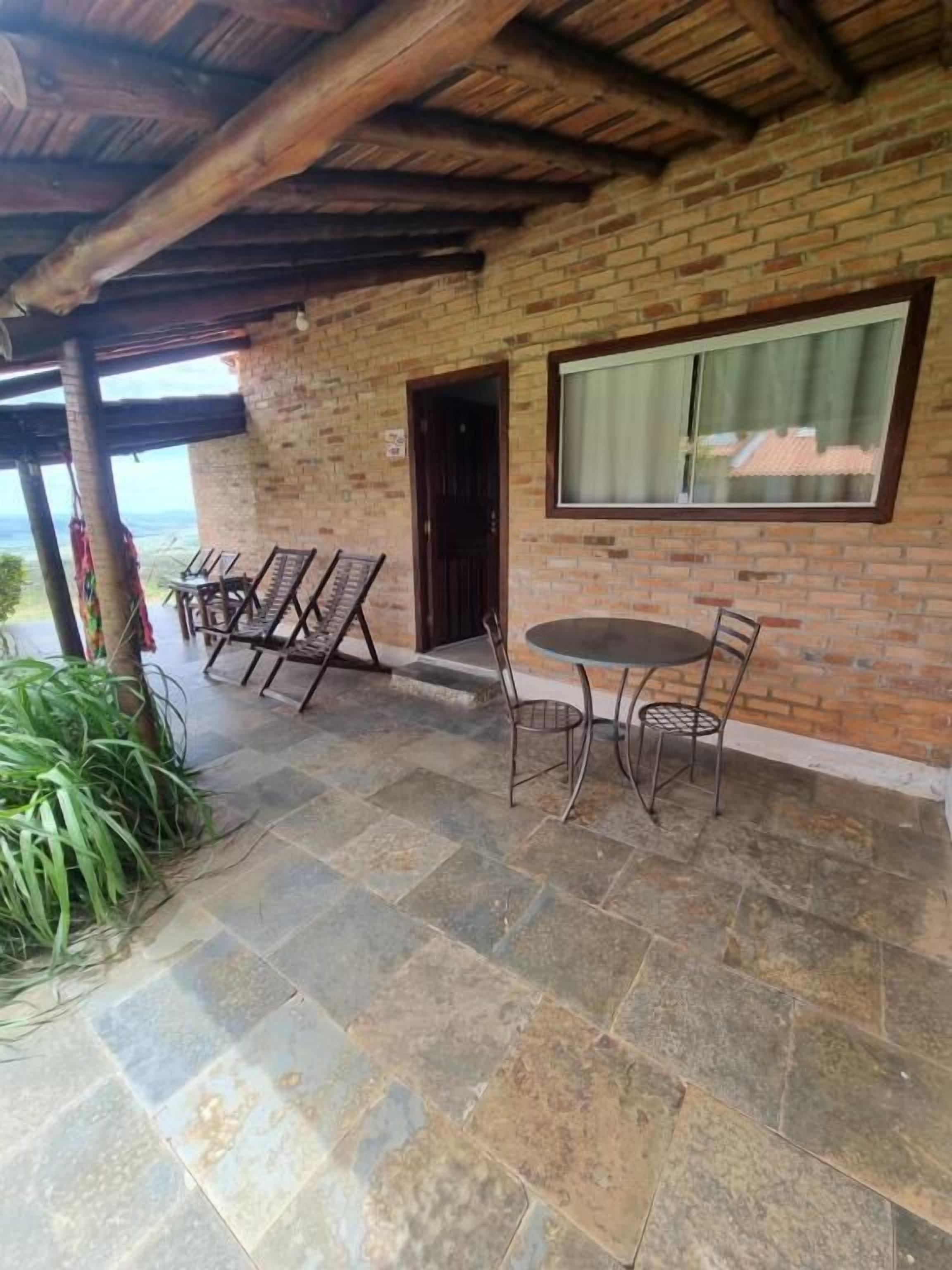 A covered patio with a brick wall, a round table with chairs, and a view of the landscape.