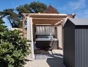 Uma área de estar coberta ao ar livre com um banco, uma mesa, uma estrutura de pérgola e um pequeno galpão.