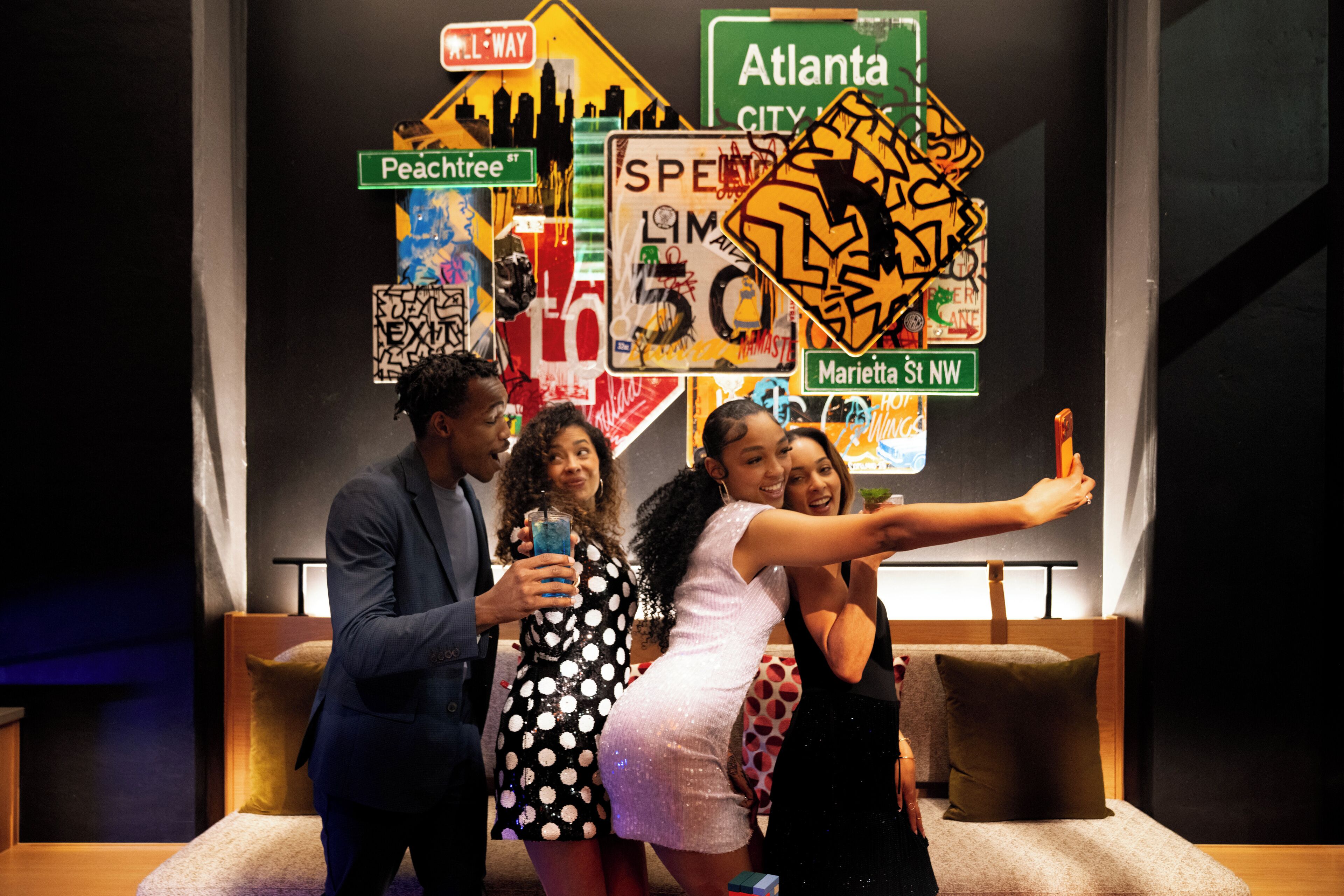 A group of people posing in front of a wall with various street signs and a city skyline silhouette.