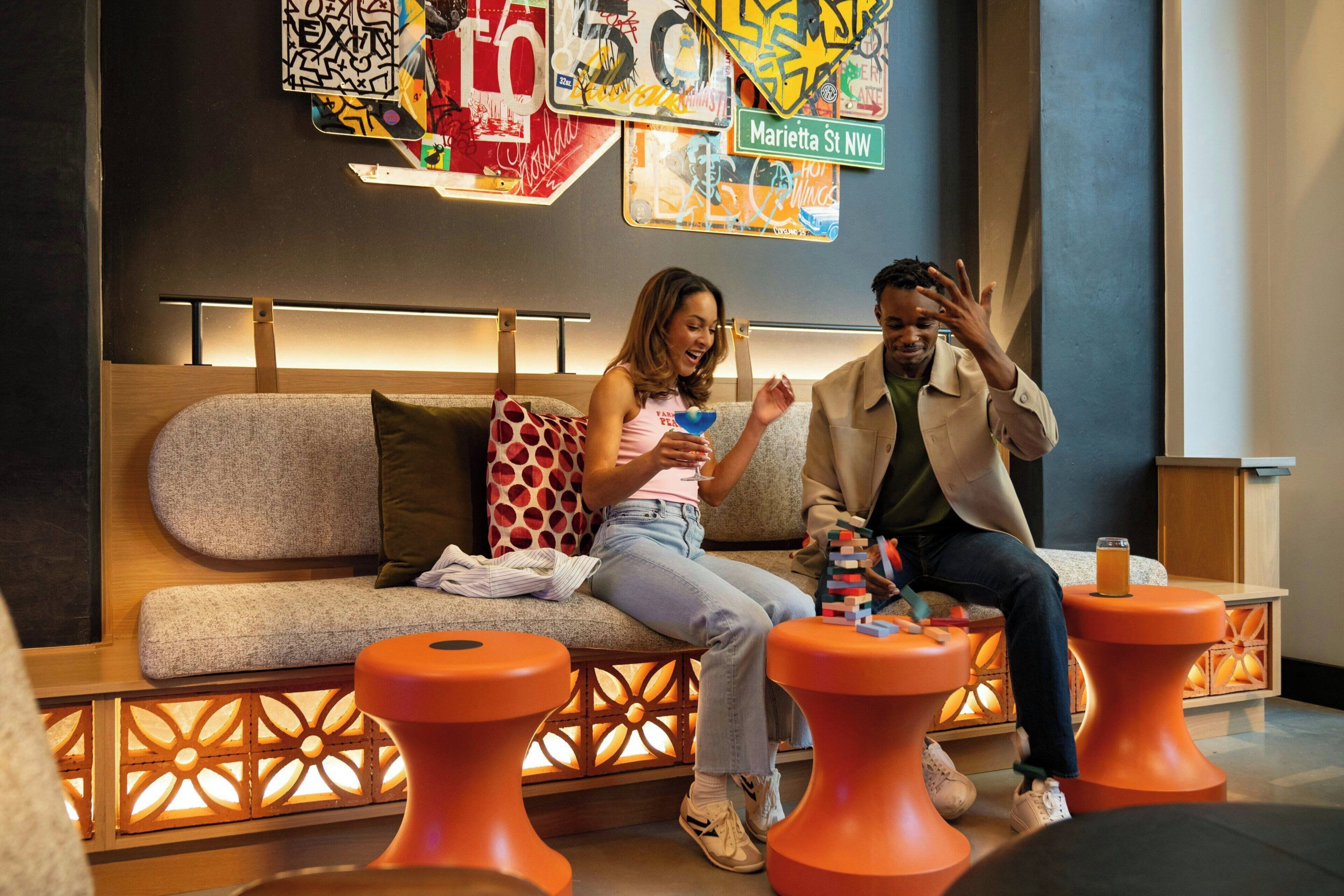 A modern lounge area with a sofa and orange stools, a wall with colorful street art, and a sign indicating 'Marietta St NW'.