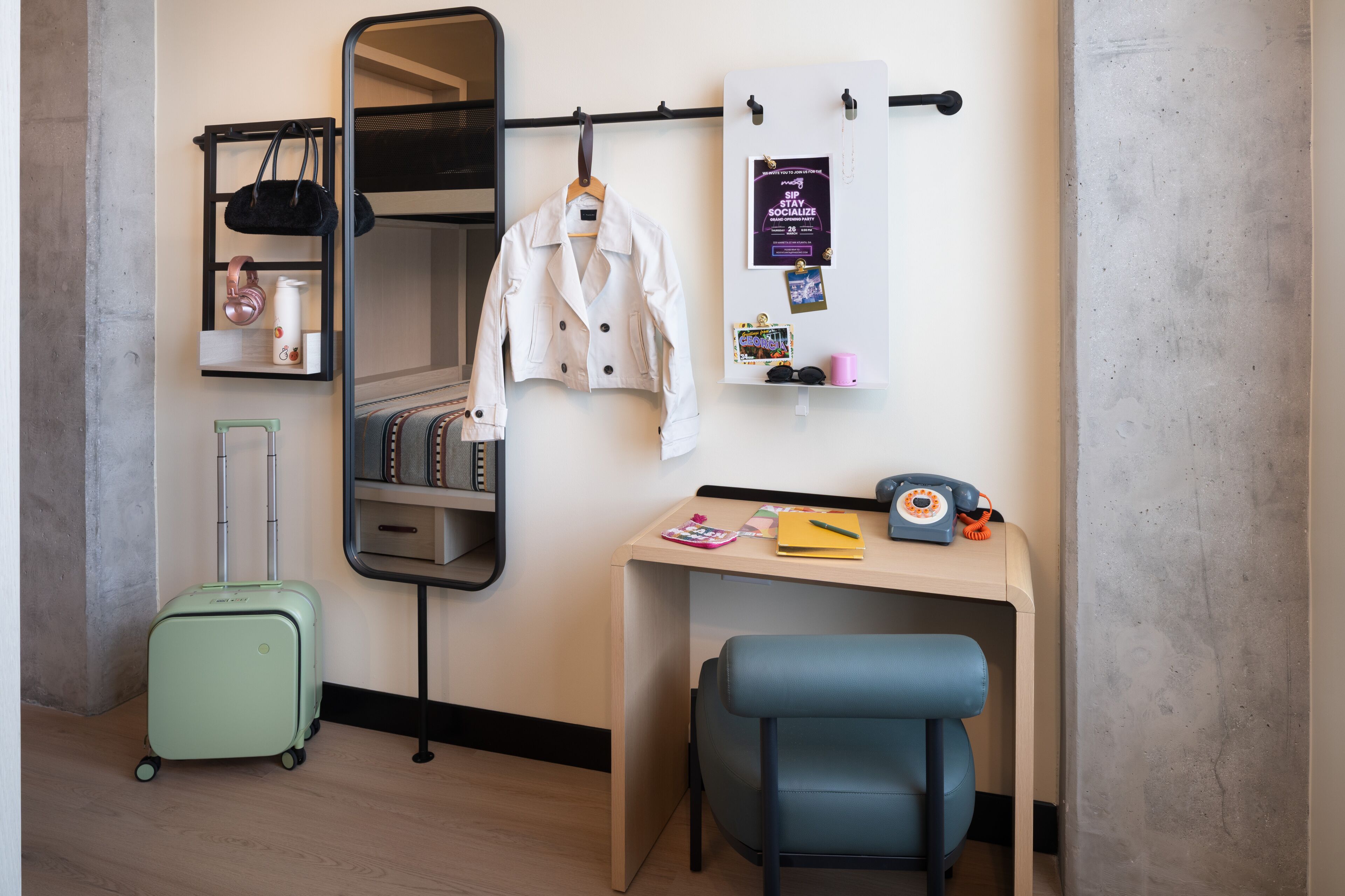 A room with a bunk bed, a desk with a chair, a suitcase, a mirror, and a bulletin board.
