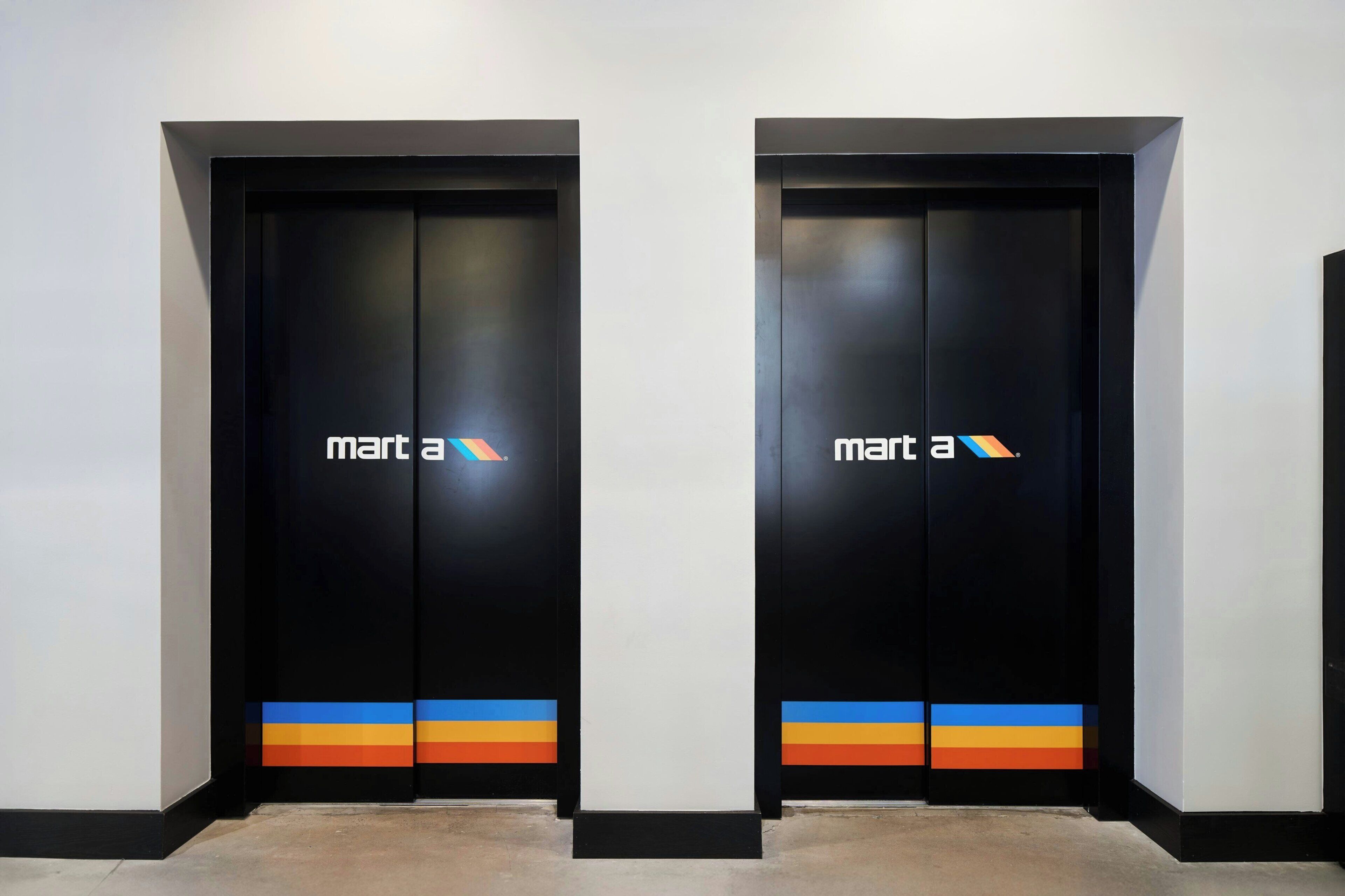 Two black doors with 'mart a' signage and a colorful stripe at the bottom.