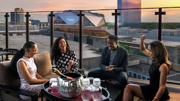 A group of people seated on a rooftop terrace with a cityscape view, including a modern building and a stadium.