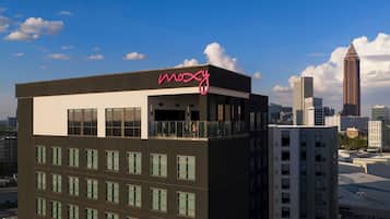 Un bâtiment moderne, surmonté d’un grand panneau lumineux portant l’inscription « Moxy », entouré d’autres immeubles de grande hauteur et se dressant sous un ciel dégagé.