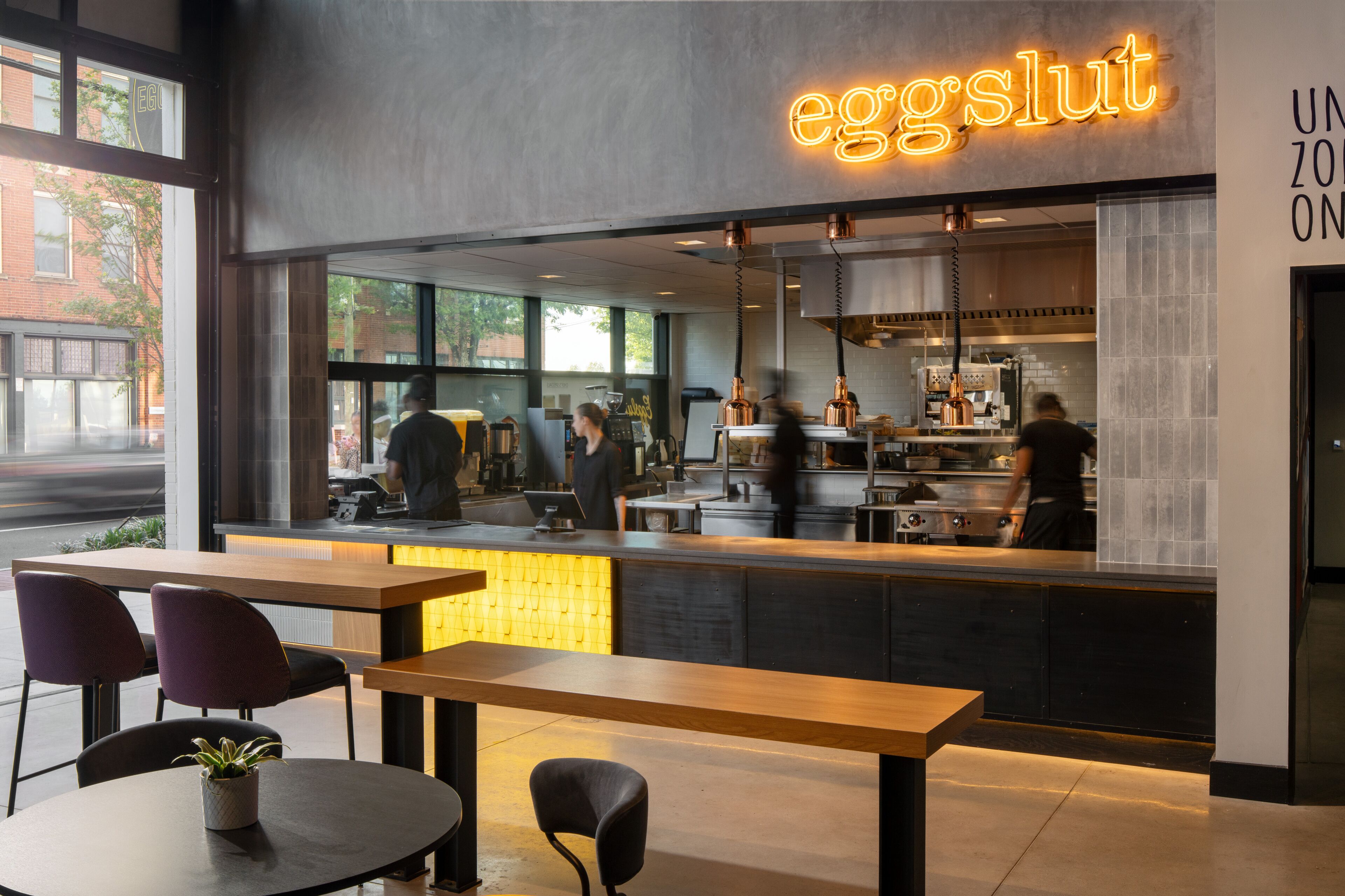 A modern cafe interior with a neon sign, seating area, and visible kitchen staff.