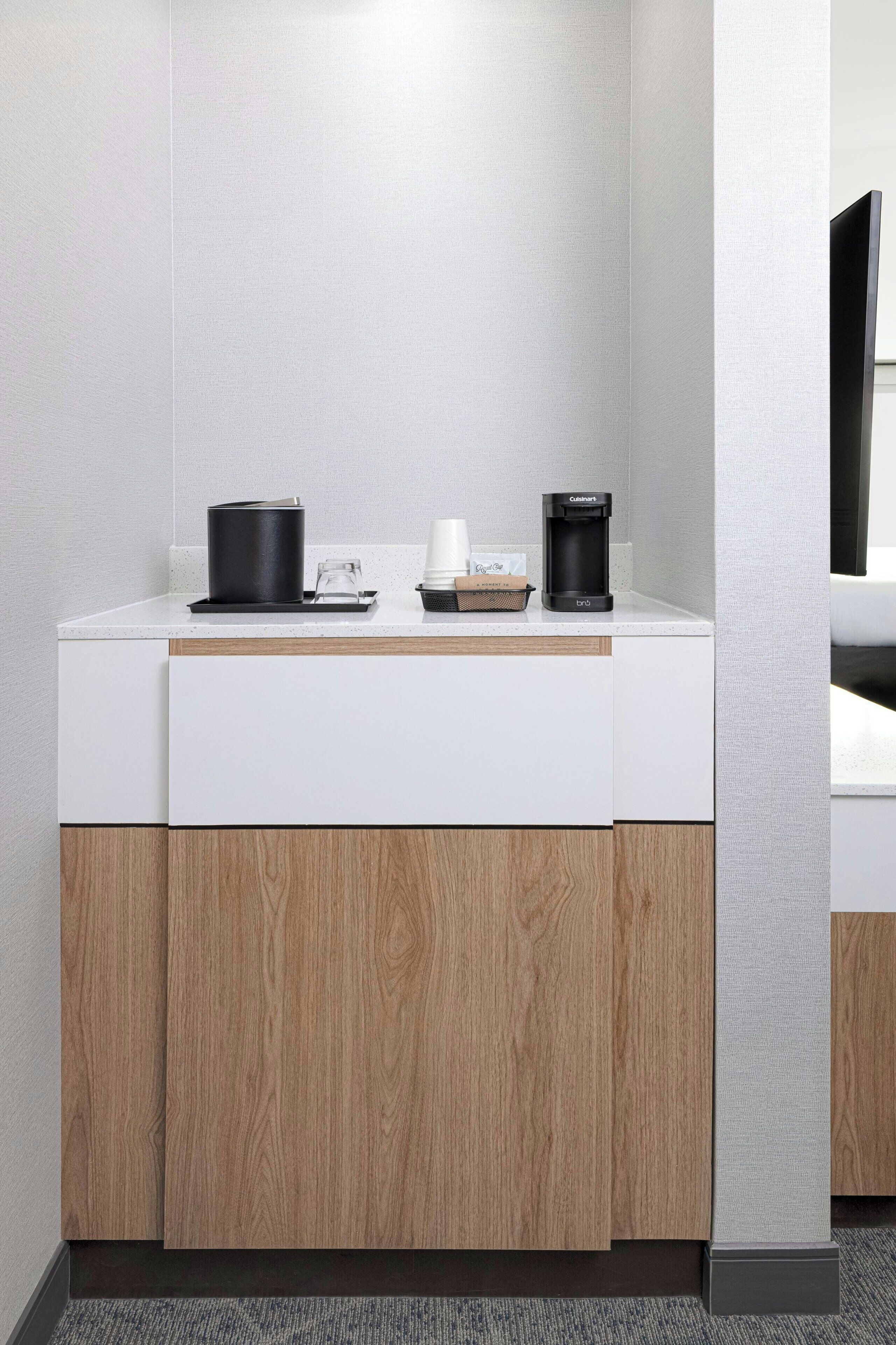 Eine moderne Küchenzeile mit einer Kaffeemaschine, einem Wasserkocher und einem Glas auf der Arbeitsfläche.