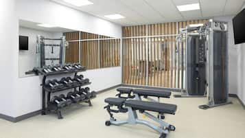 Un gimnasio con equipo de levantamiento de pesas, bancos y un muro con espejos.