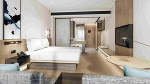 Une chambre d’hôtel moderne avec un grand lit, un coin salon avec une table ronde, une télévision et une salle de bain équipée d’un miroir et d’un lavabo.
