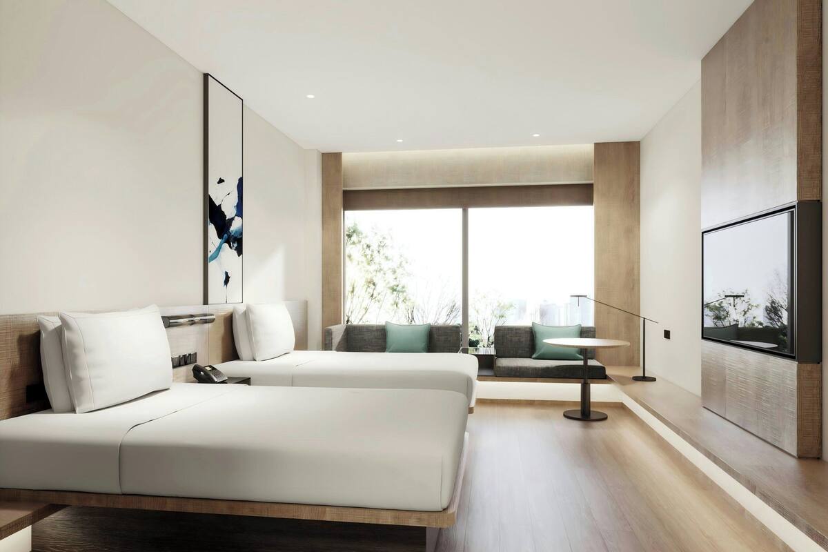 Habitación de hotel moderna con una cama grande, un área de descanso con una mesa y un ventanal que ofrece vistas al exterior.