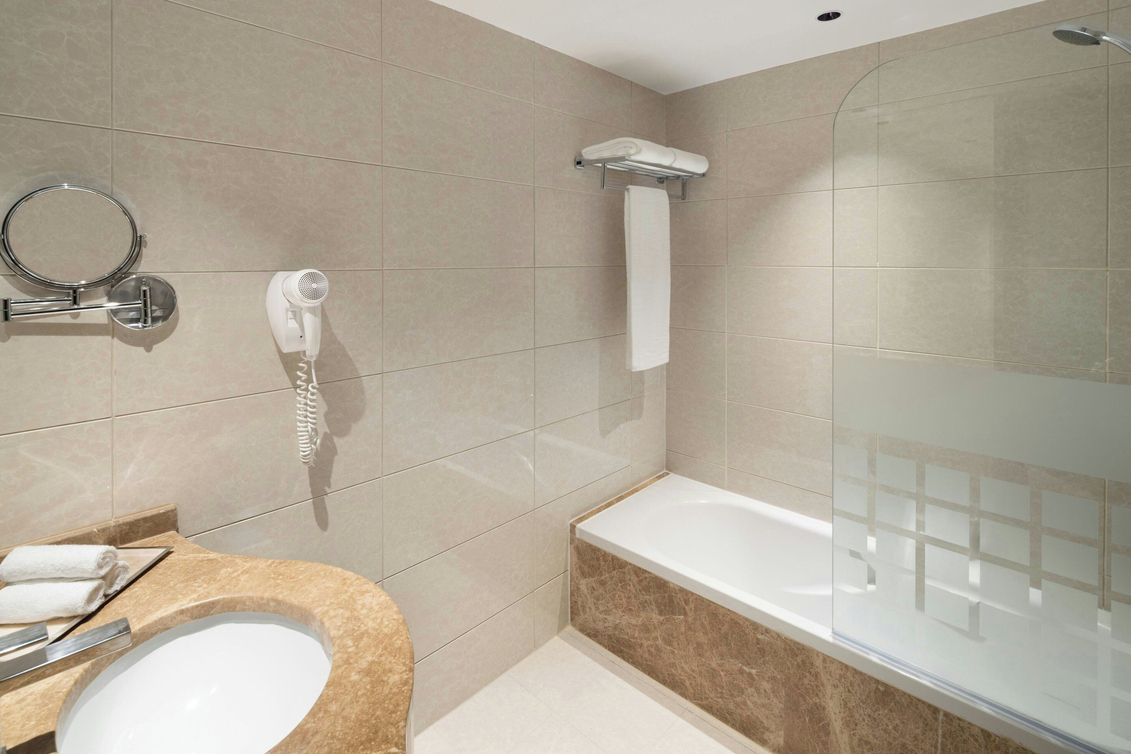 A modern bathroom with a sink, mirror, hairdryer, and a glass-enclosed shower area.