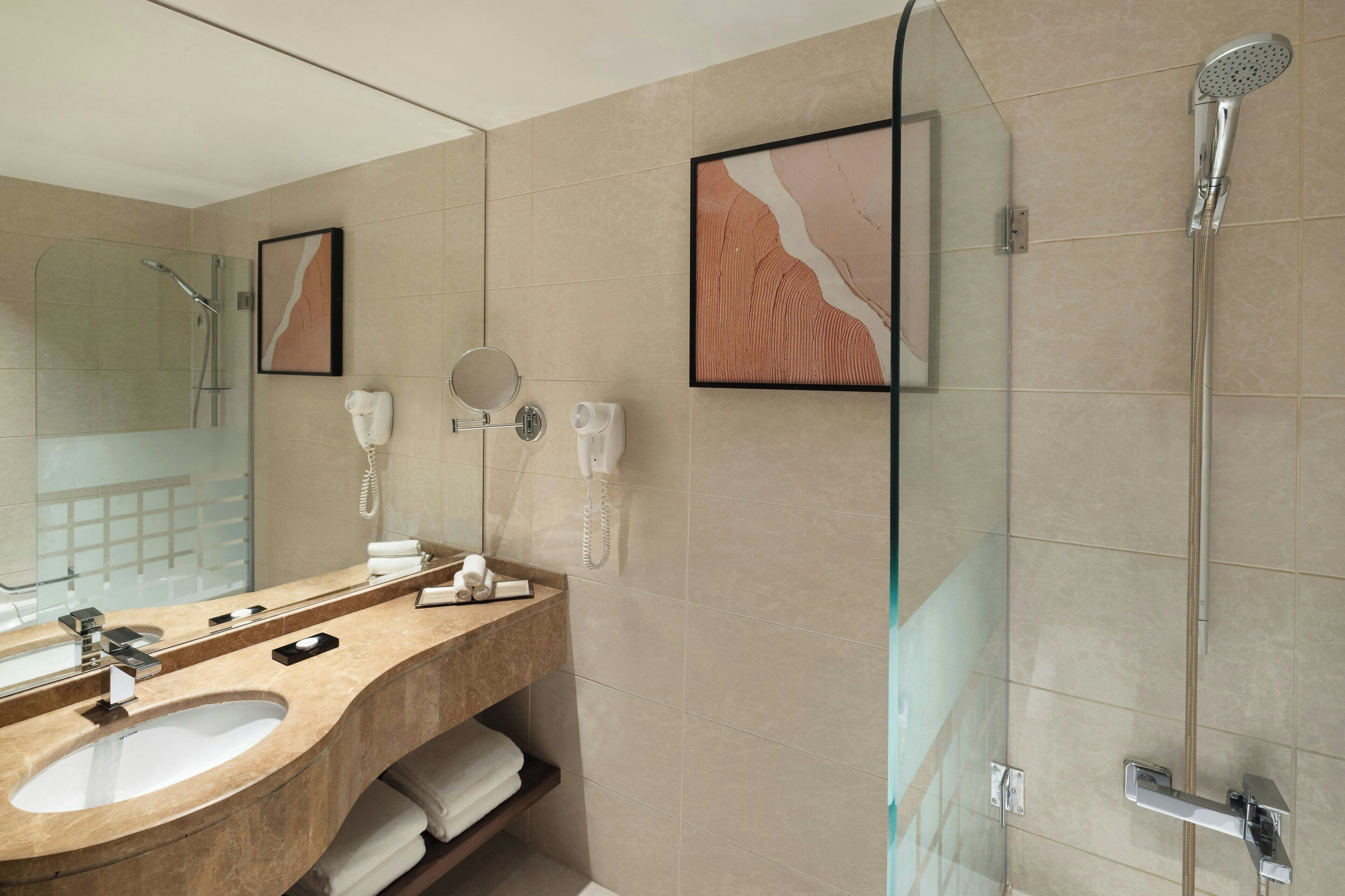 A modern bathroom with a large mirror, two sinks, a shower, and a towel rack.