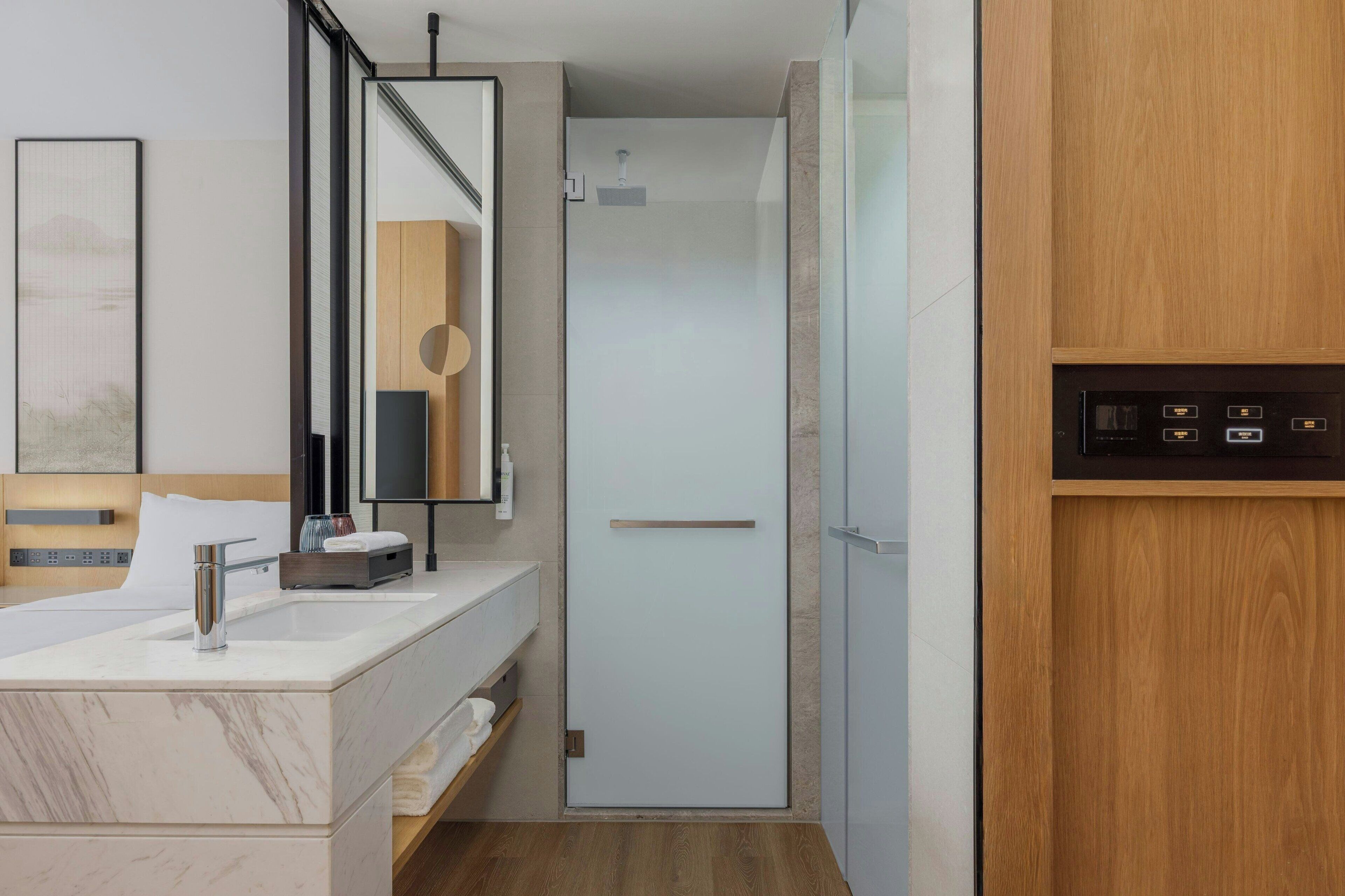 A modern bathroom with a marble sink, a large mirror, a wooden vanity, and a shower area.