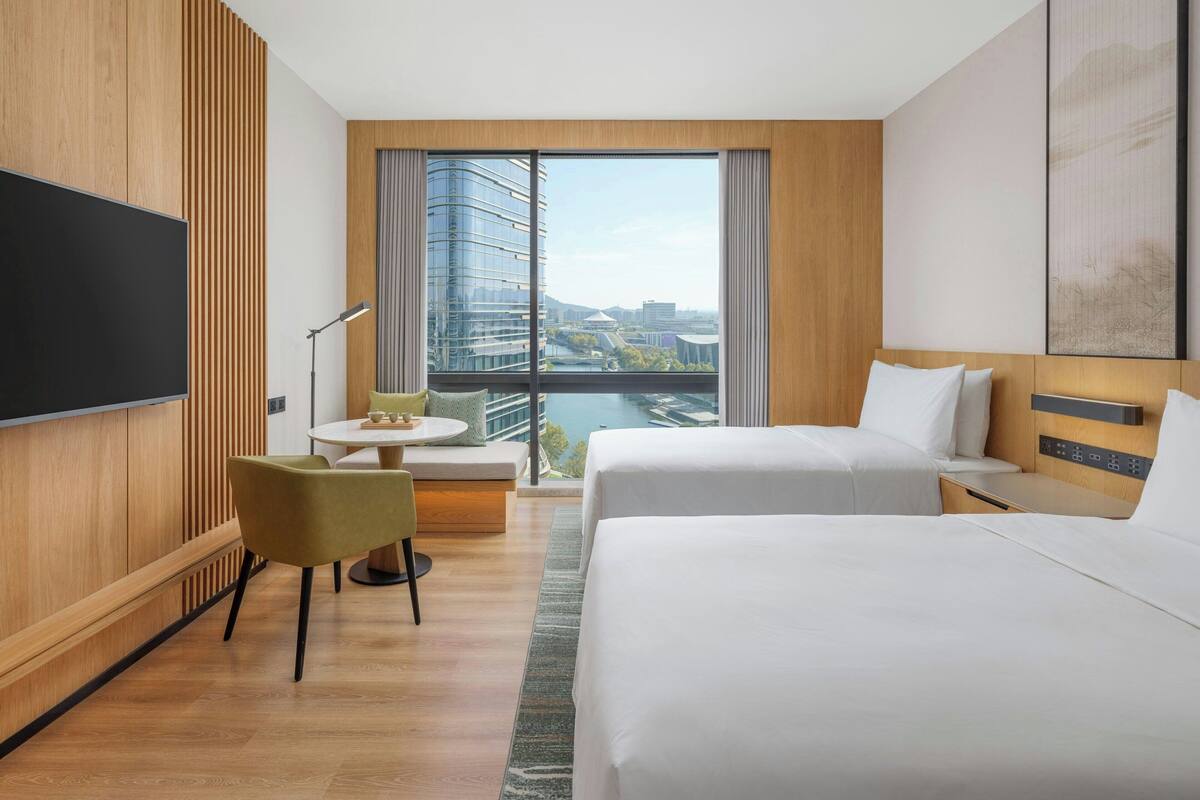 Une chambre d’hôtel avec deux lits, une télévision, un bureau avec une chaise et une vue sur le paysage urbain.