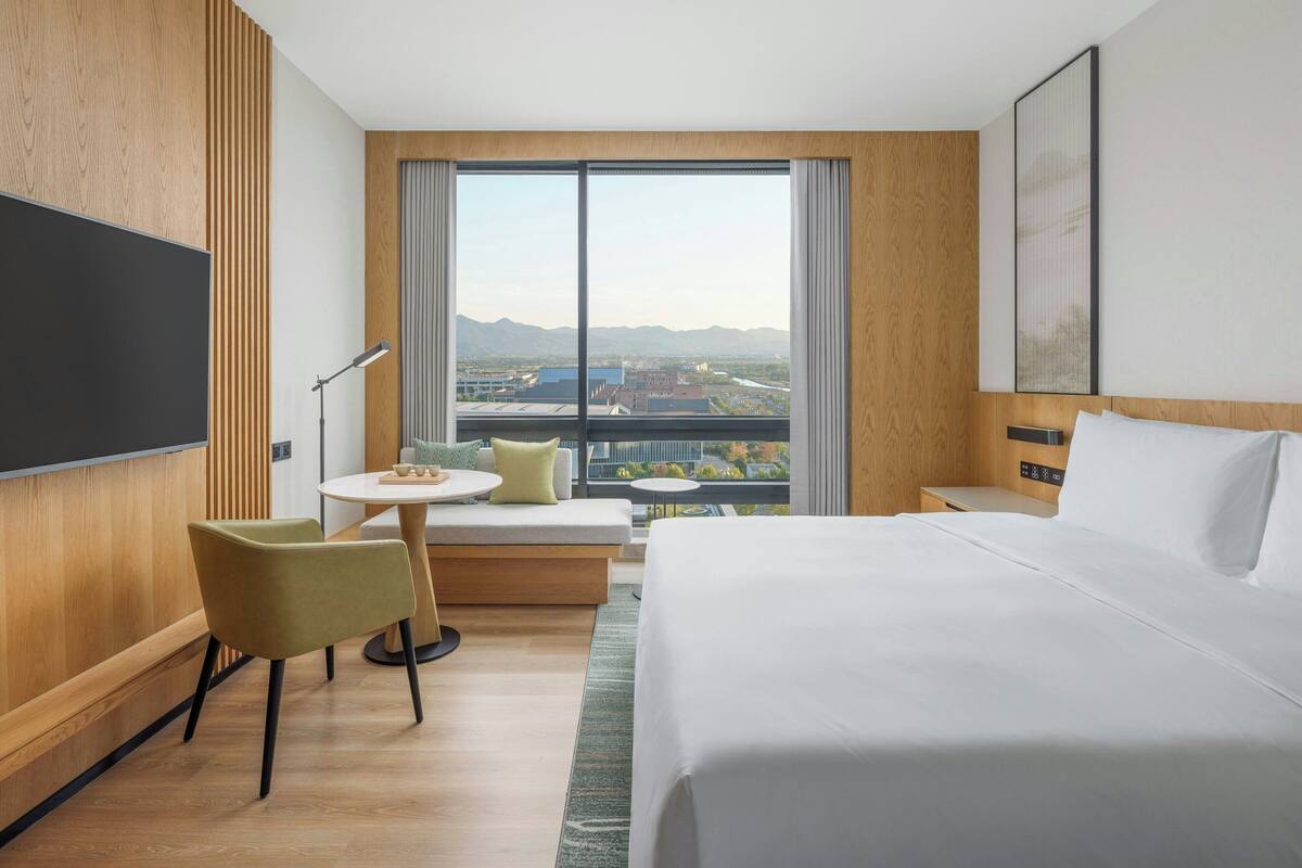 Une chambre d’hôtel avec un grand lit, un bureau avec une chaise, une télévision et une vue sur le paysage urbain.