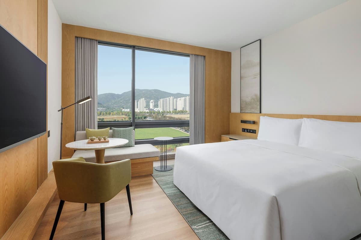 Une chambre d’hôtel avec un grand lit, un coin salon avec une table, une télévision et une fenêtre donnant sur la ville.