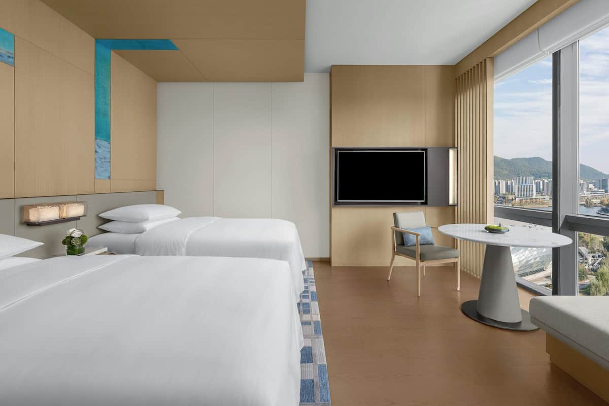 Ein Hotelzimmer mit zwei Betten, einem Fernseher, einem kleinen Tisch und Blick auf die Stadt.