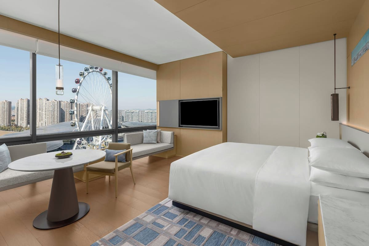 Ein modernes Hotelzimmer mit einem großen Bett, einem runden Esstisch, einer Couch und einem Fernseher.