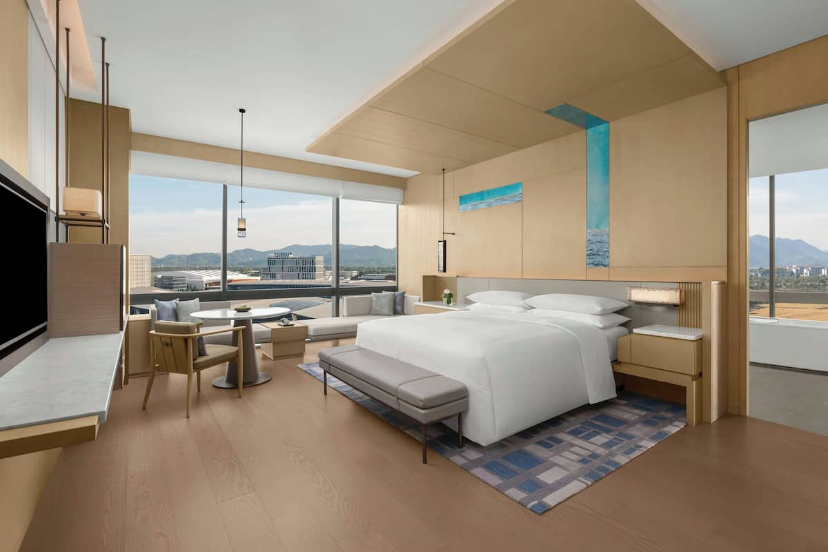 Ein modernes Hotelzimmer mit einem großen Bett, einer Sitzecke, einem Schreibtisch und einem Fernseher.