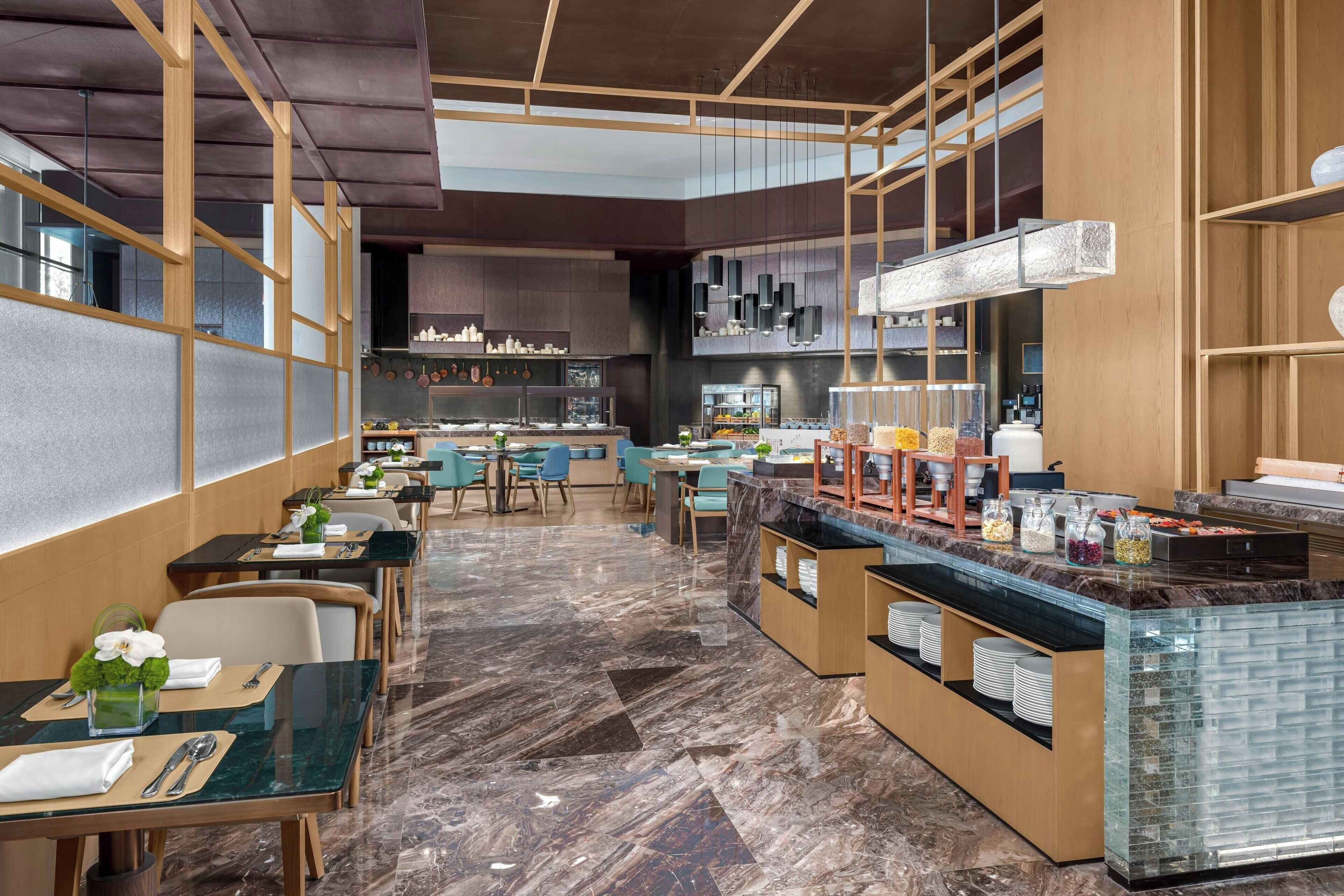 A modern restaurant with a long counter, seating area, and kitchen in the background.
