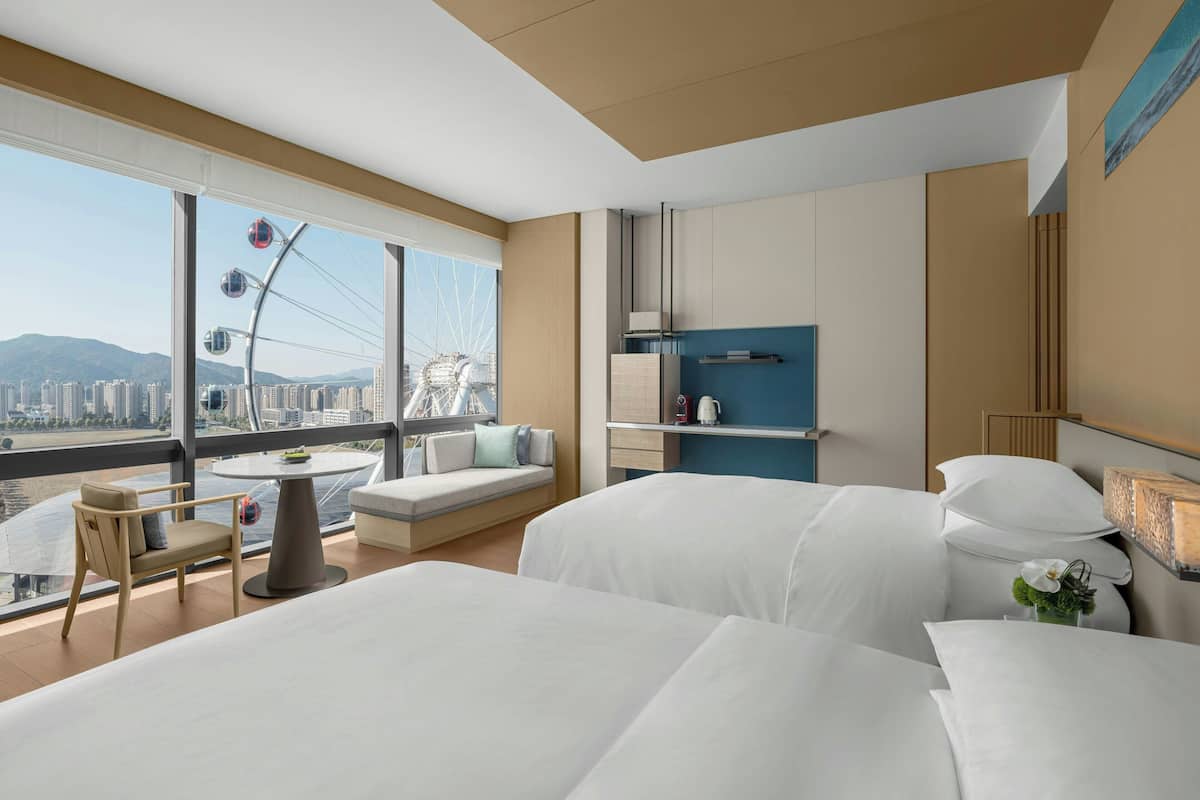 Ein modernes Hotelzimmer mit großem Fenster, einer Couch, einem Esstisch und einem Bett.