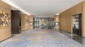 Een moderne hotelgang met een kamerbreed tapijt, houten paneelwanden en een glazen deur aan het einde.