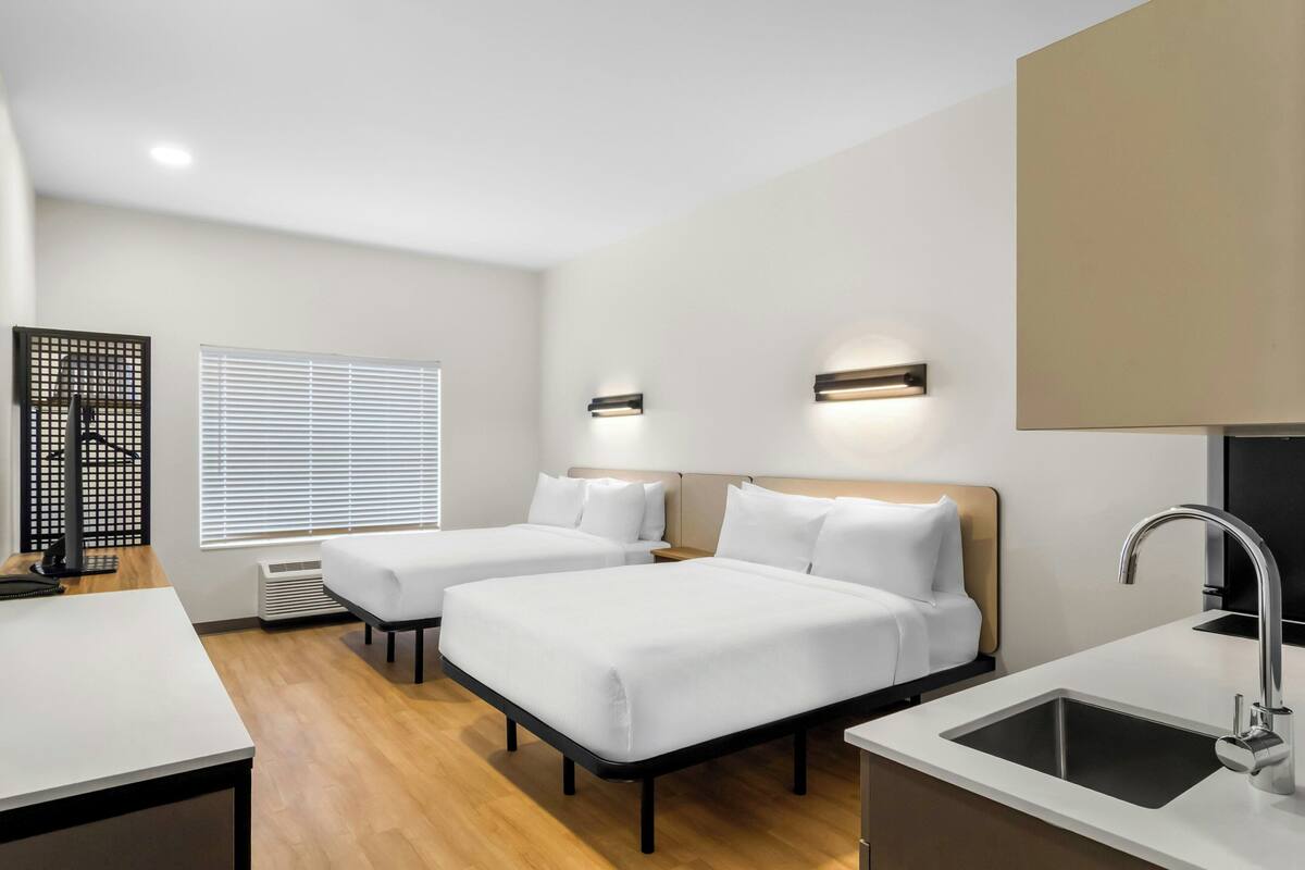 Une chambre d’hôtel moderne équipée de deux lits, d’un bureau, d’un lavabo et d’une fenêtre avec des stores.