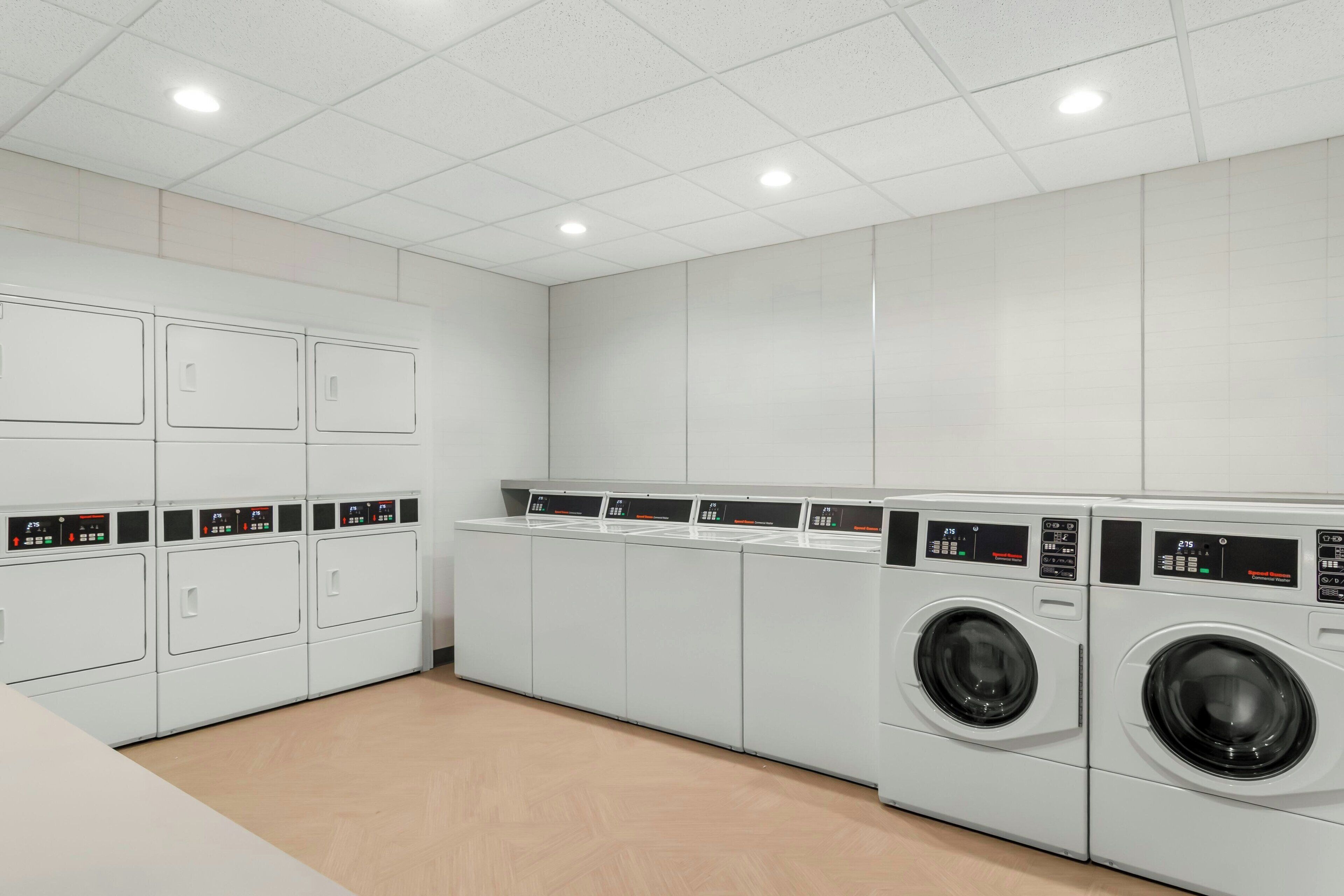 A laundry facility with multiple washing machines and dryers, white tiled walls, and a wooden floor.