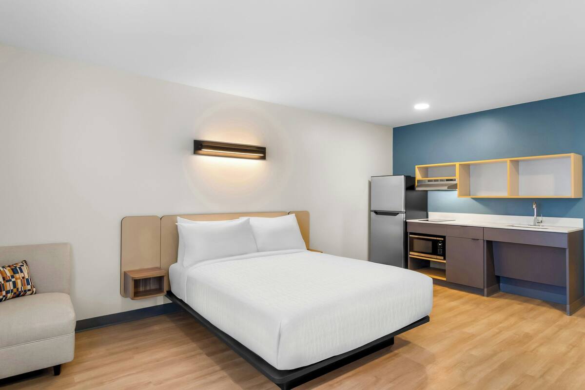 Une chambre d’hôtel moderne équipée d’un lit, d’un petit canapé, d’une kitchenette et d’une lampe fixée au mur.
