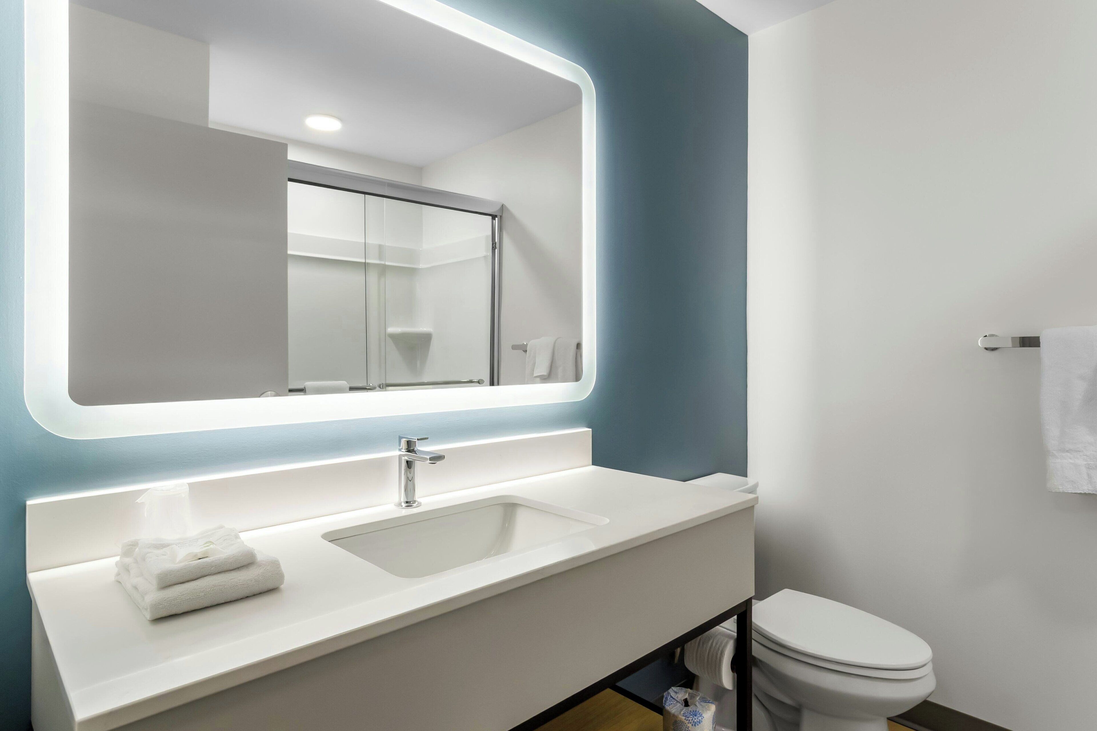 A modern bathroom with a large mirror, white sink, and toilet.