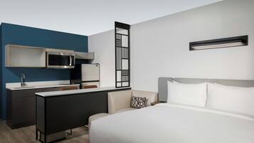 Een moderne hotelkamer met een bed, een bureau met een magnetron, een klein keukentje en een decoratieve roomdivider.