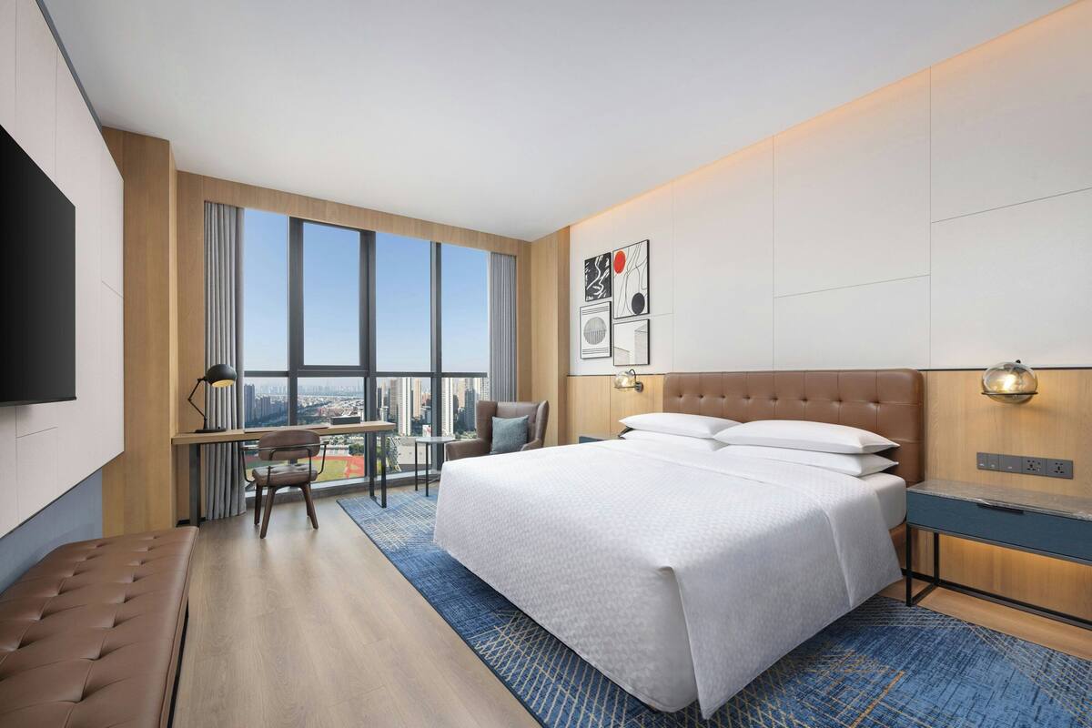 A modern hotel room with a large bed, a desk, a chair, and a TV.