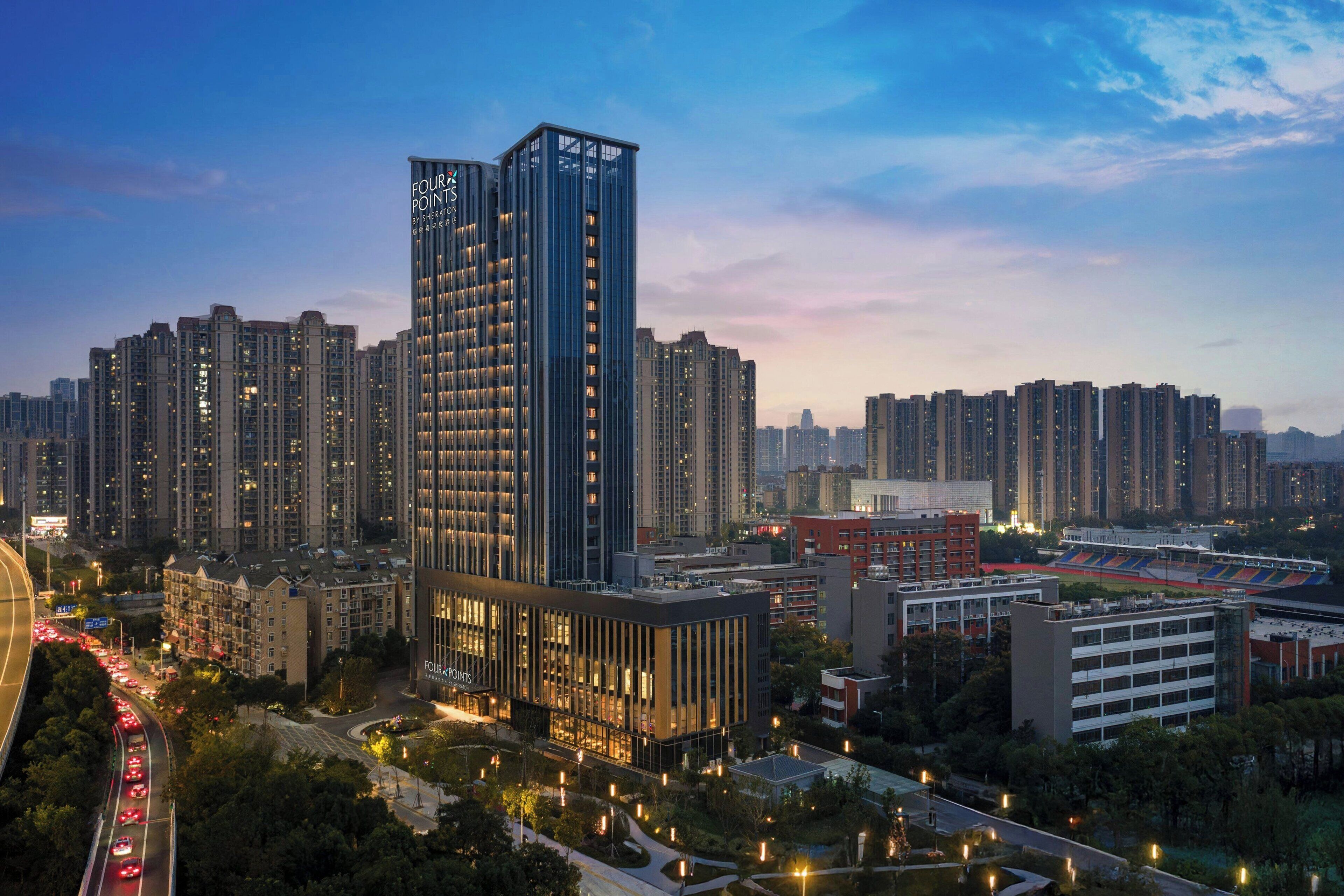 A high-rise building with a modern design, surrounded by other high-rise buildings and a sports stadium.
