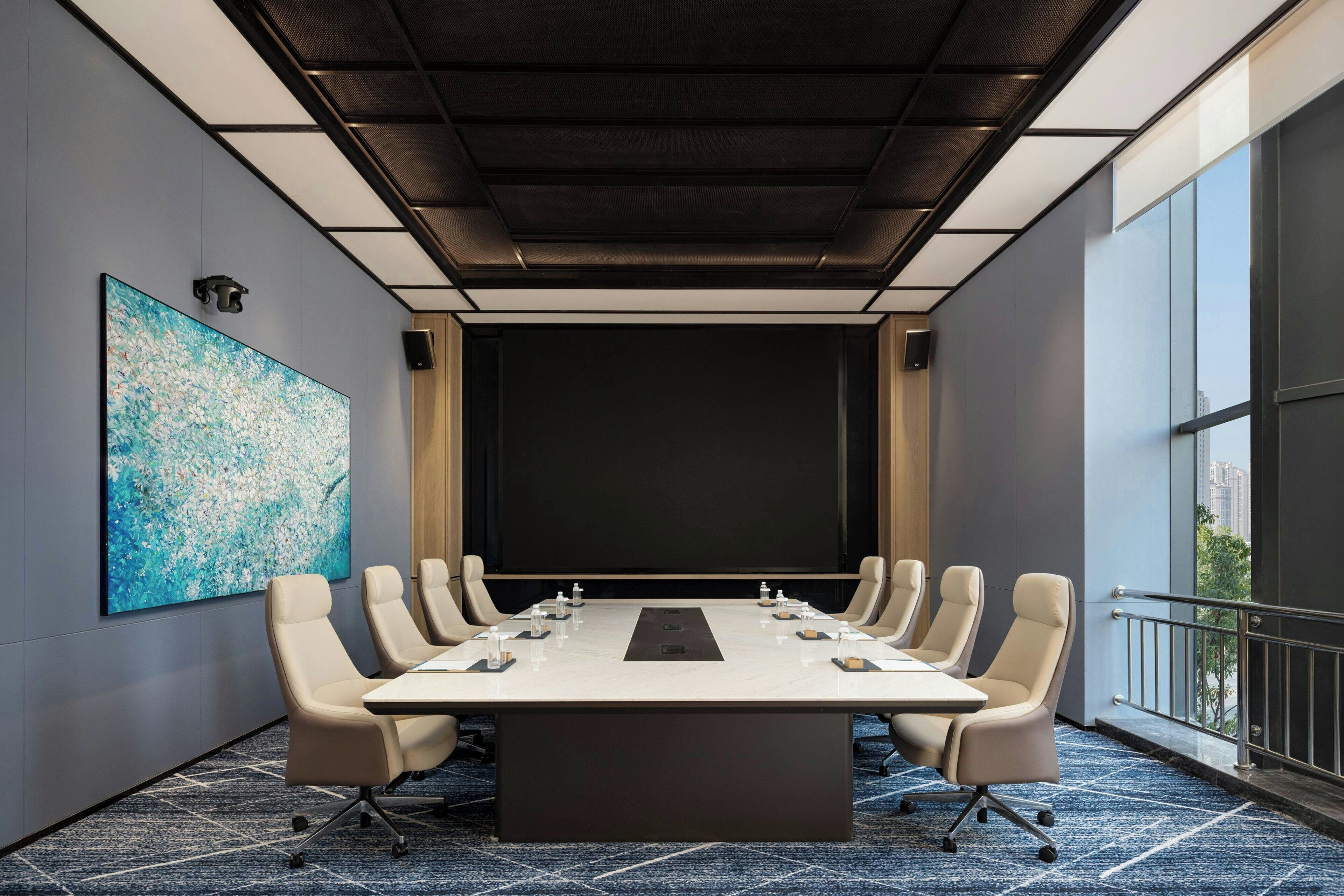 A conference room with a long table, six chairs, and a large screen.