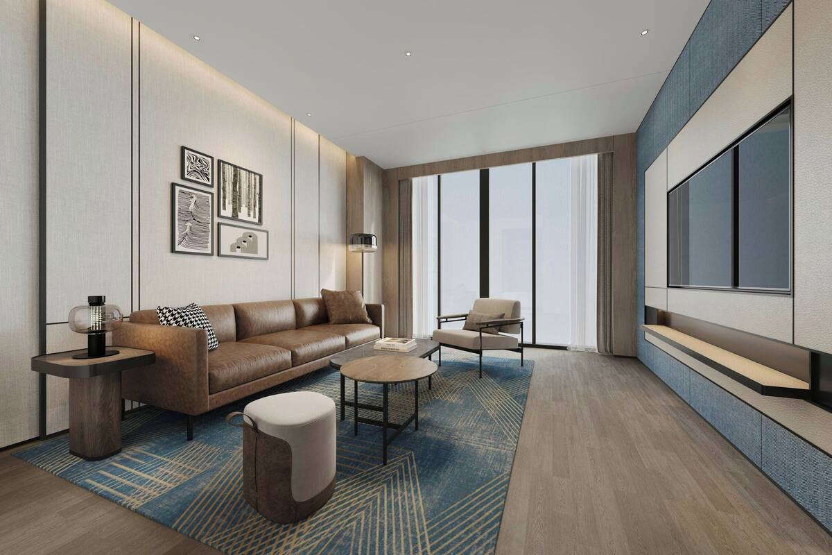 A modern living room with a brown leather sofa, a round coffee table, a side table with a lamp, and a large TV on the wall.