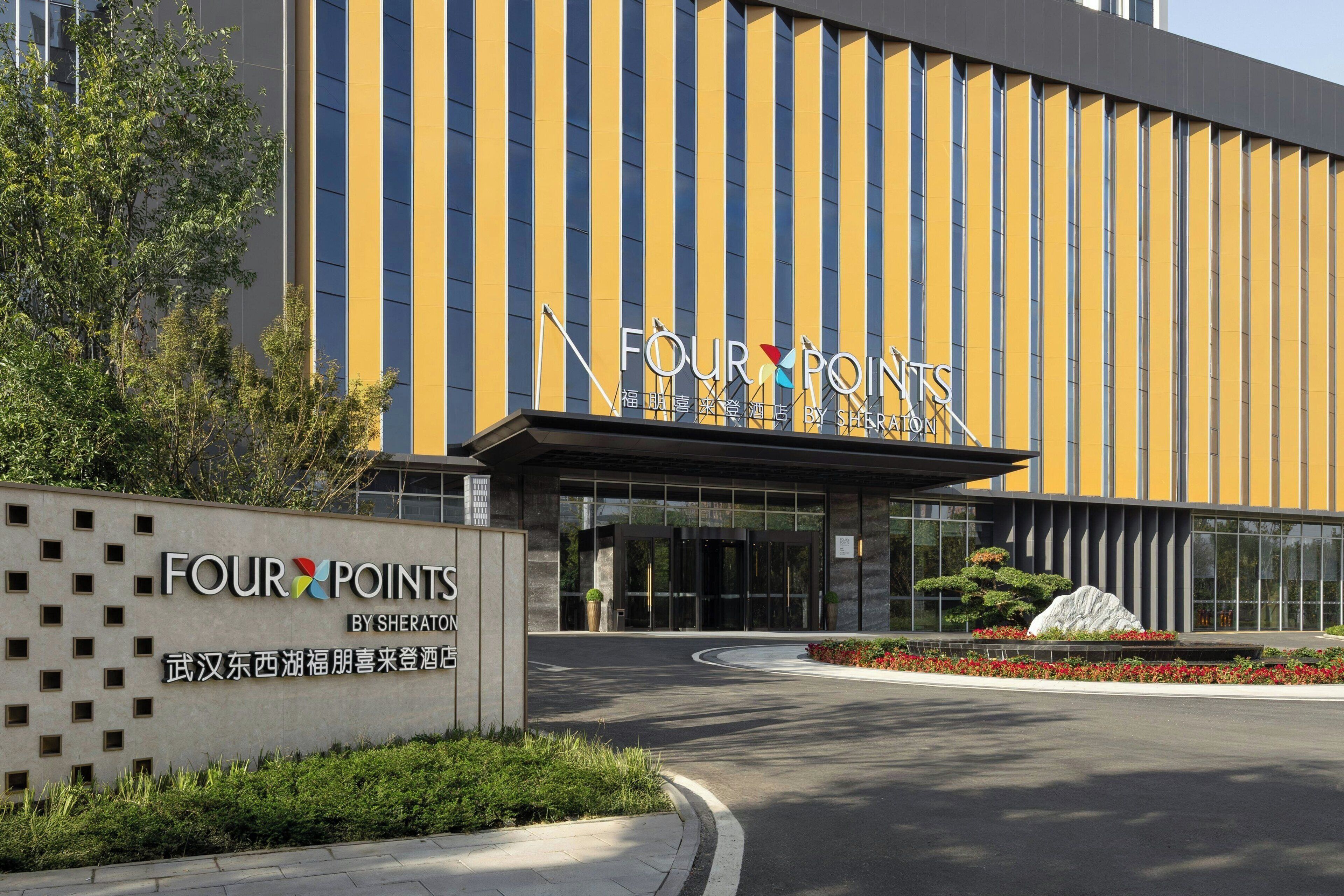 A hotel entrance with a modern facade, large glass doors, and a sign reading "FOUR POINTS BY SHERATON".