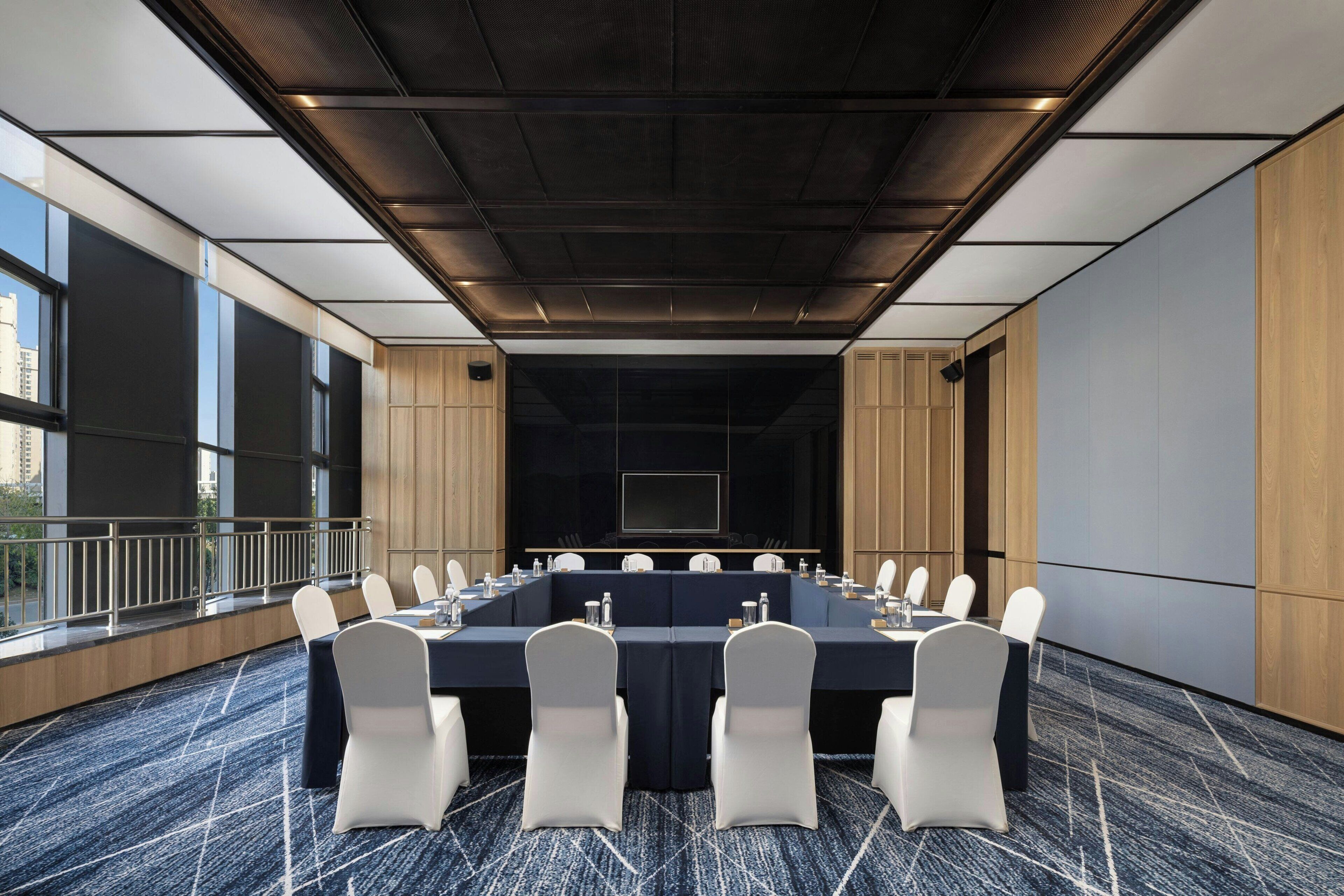 A conference room with a long table, white chairs, and a large screen at the front.