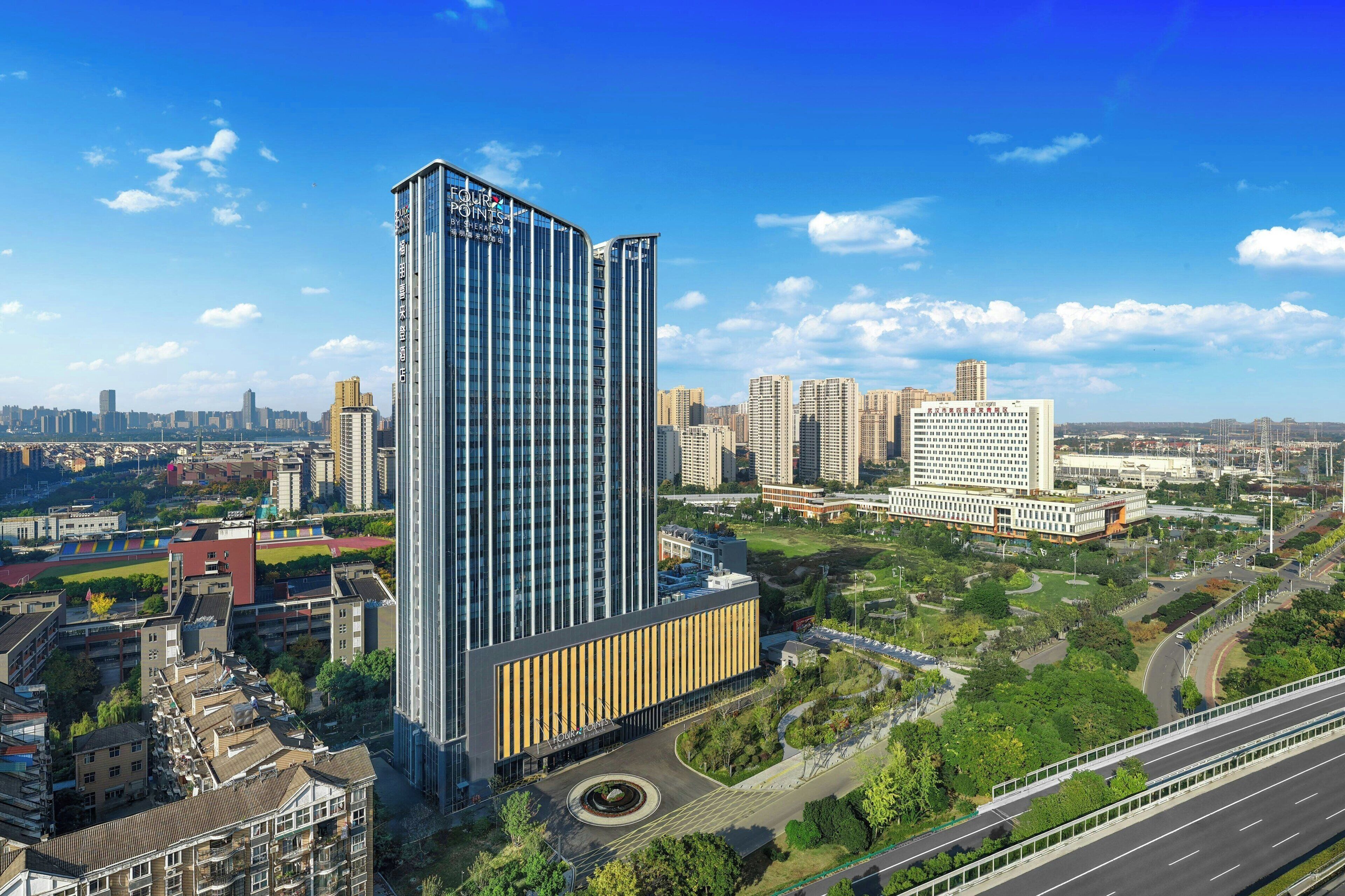 Un edificio moderno de gran altura, rodeado por un parque urbano bien cuidado y una calle con mucho tráfico.
