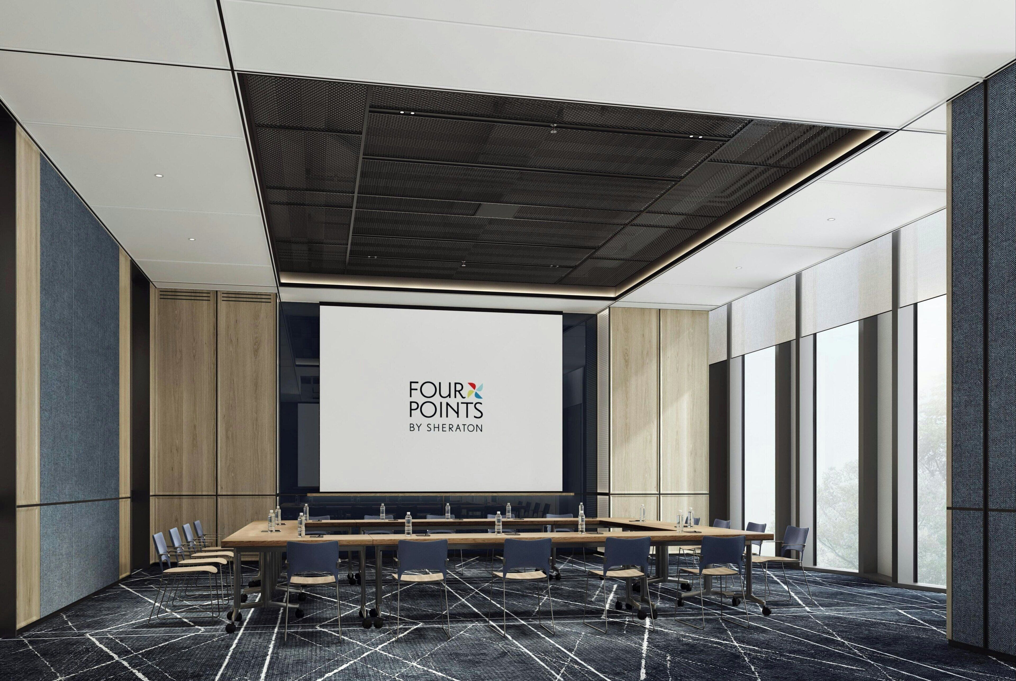 Une salle de conférence équipée d’une longue table, de chaises et d’un écran de projection affichant le logo « FOUR POINTS BY SHERATON ».