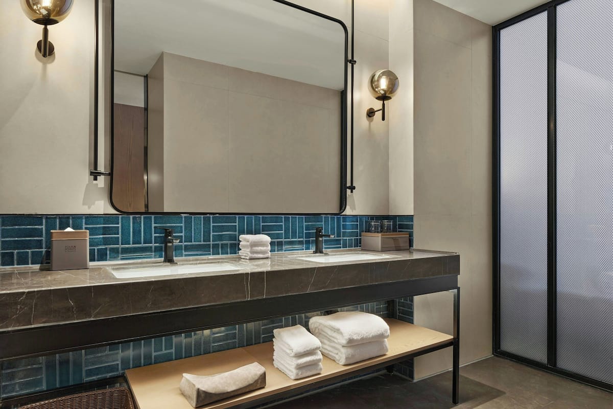 Un baño moderno con dos lavamanos, un espejo grande y un banco con toallas.
