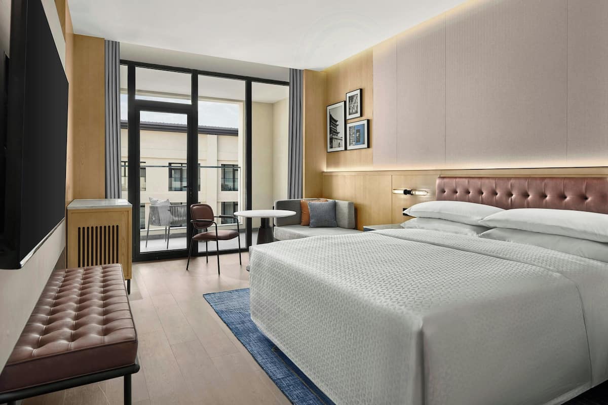 Habitación de hotel con una cama grande, un banco, una mesita y vistas al exterior.