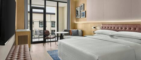 A hotel room with a large bed, a bench, a small table, and a view of the outside.