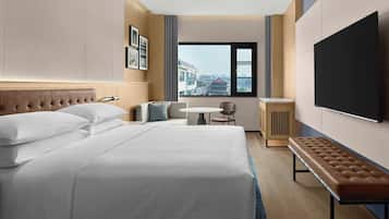 Camera d'albergo con un letto grande, un tavolino con una sedia, una panca, una TV e una finestra vista città.
